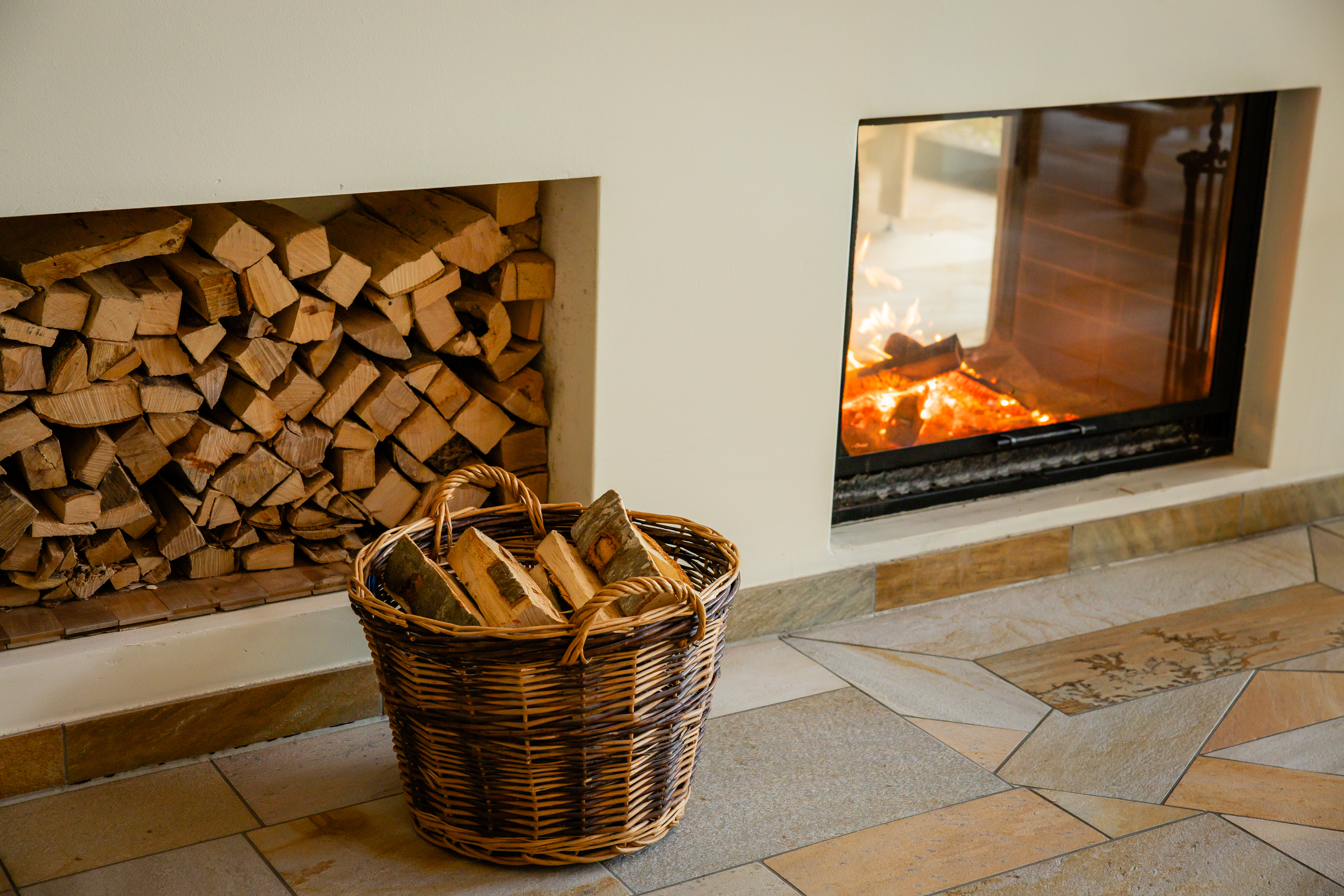 Fireplace with burning fire next to stacked wood and a basket in a cosy interior.