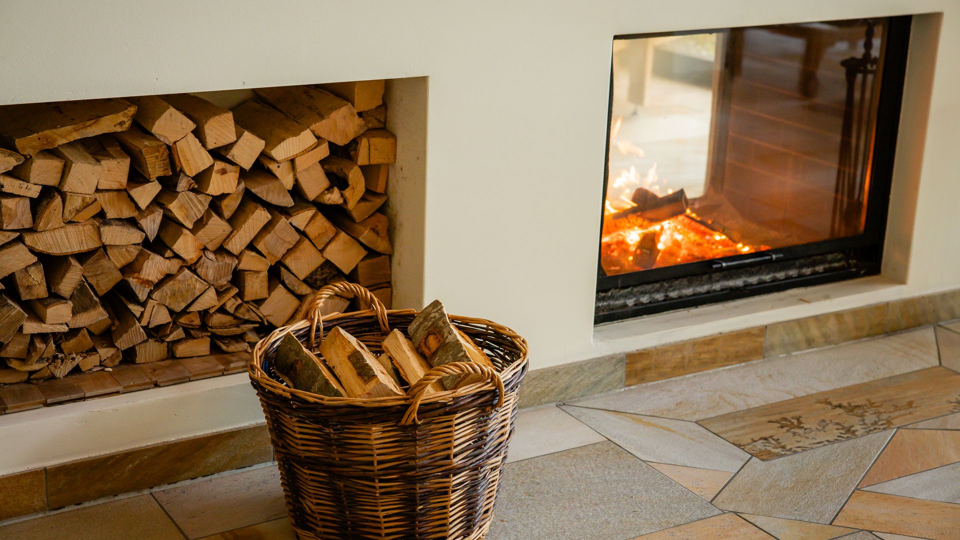 Fireplace with burning fire next to stacked wood and a basket in a cosy interior.