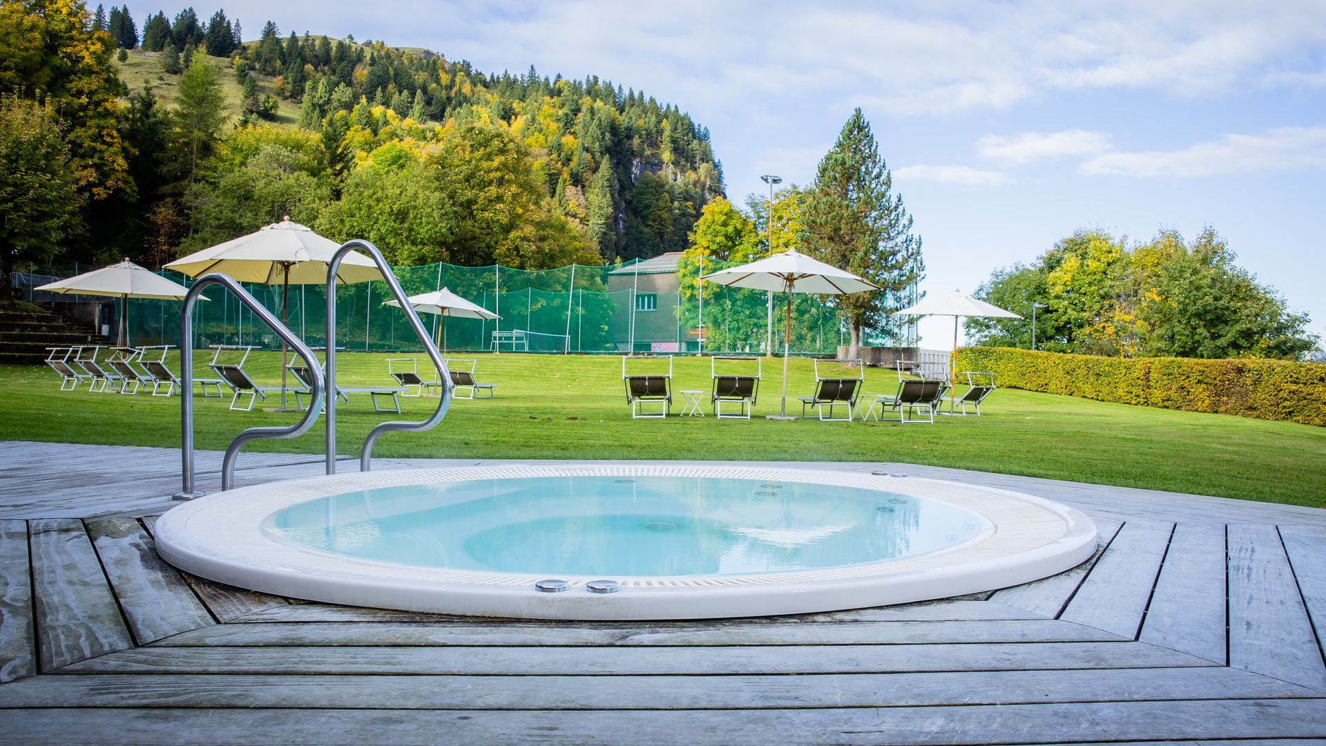 Round outdoor hot tub on a wooden deck with a view of green meadows and trees.