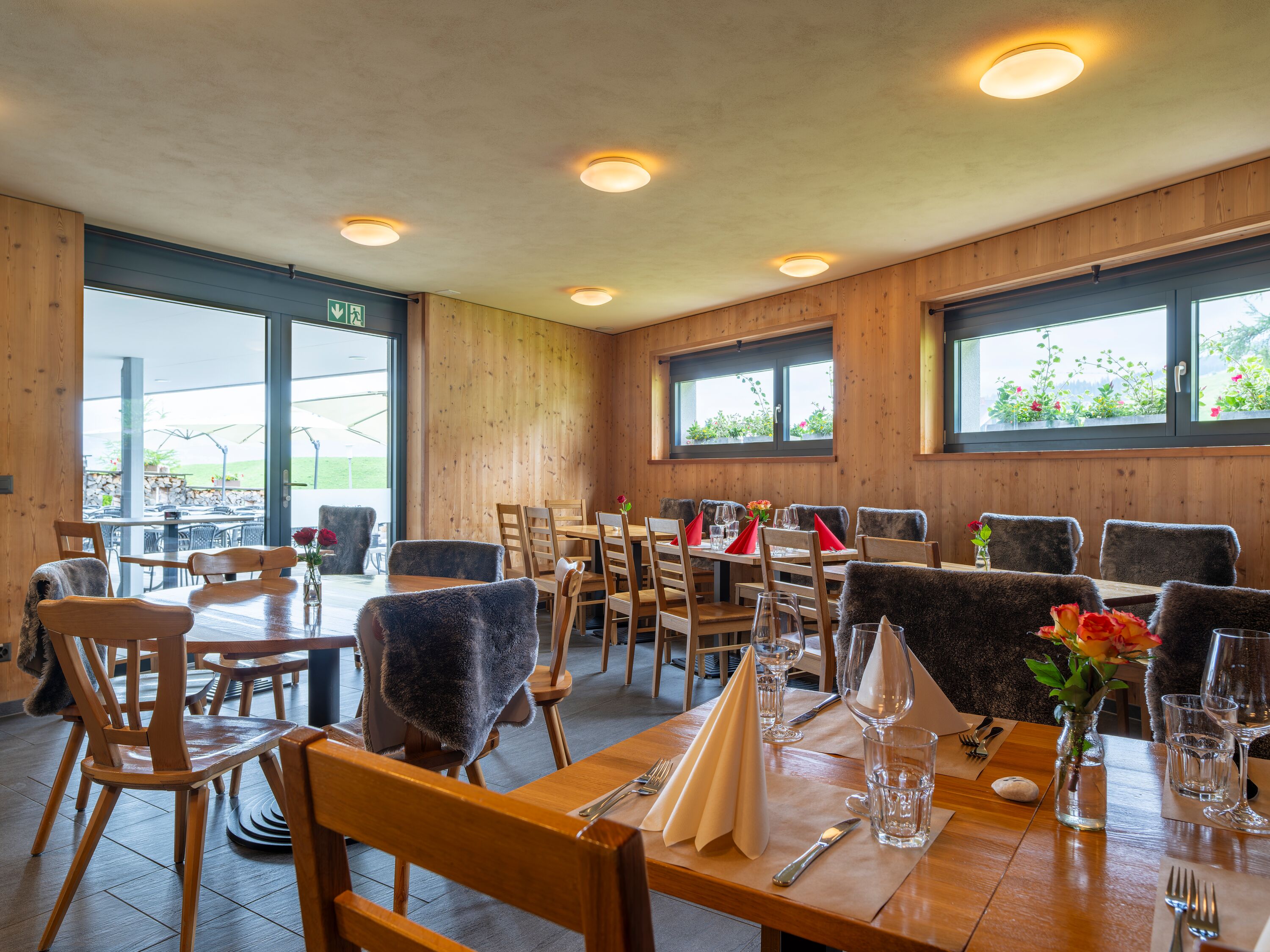 Restaurantinnenraum mit gedeckten Tischen und Blick durch grosse Fenster auf die Berglandschaft.