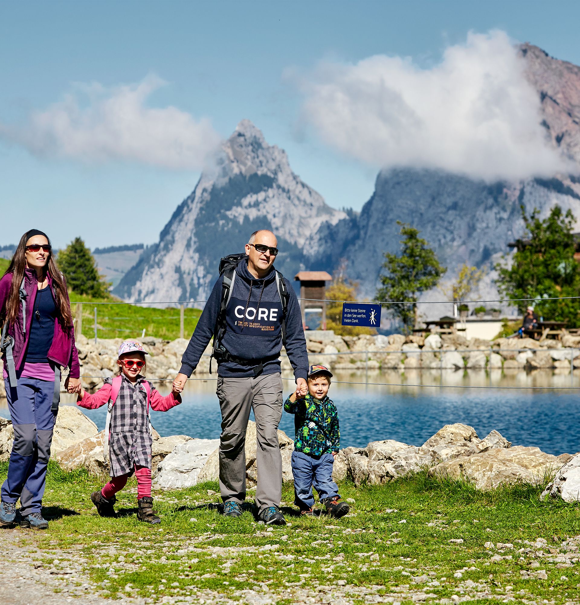 Family walking along a mountain lake with views of the surrounding mountains.