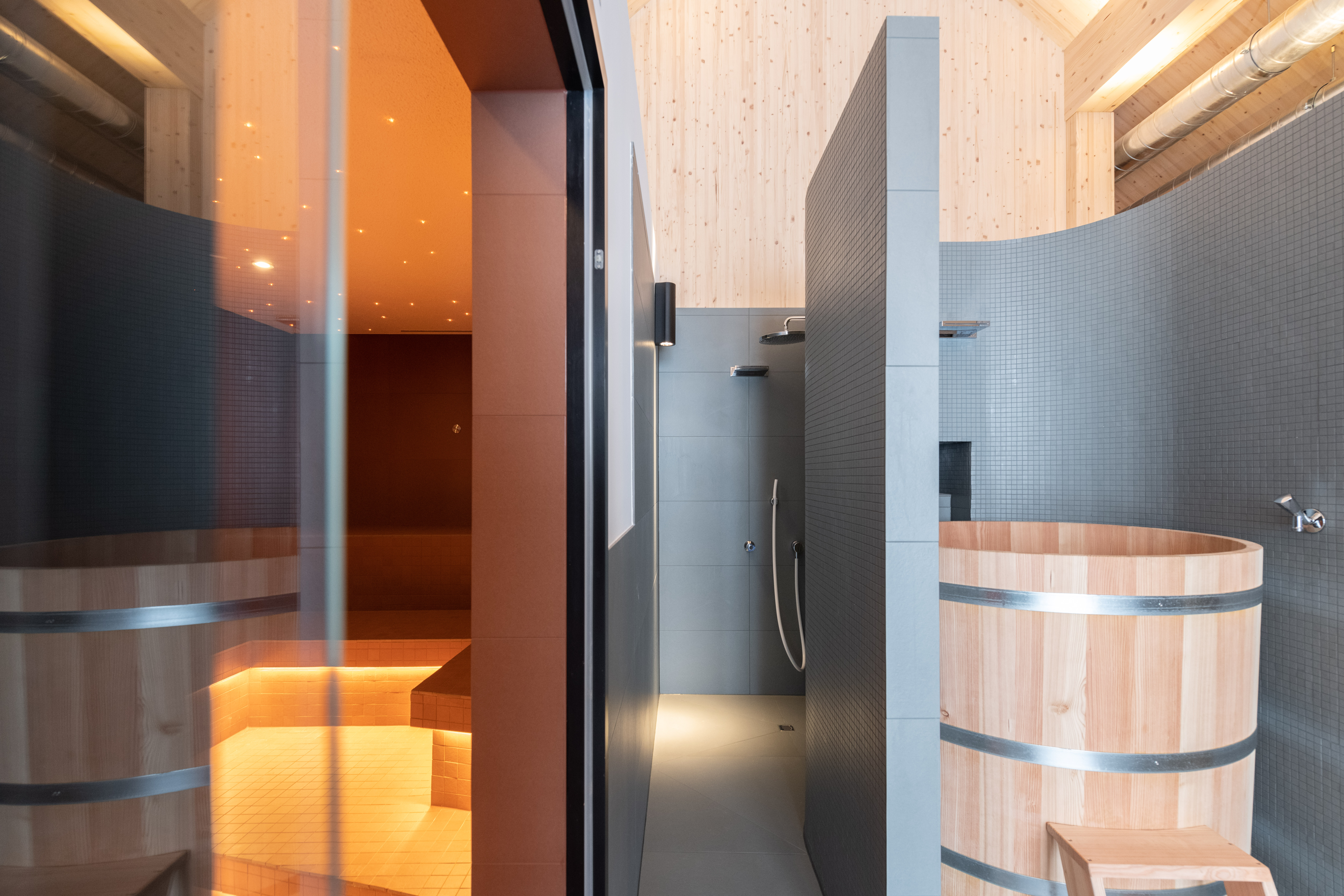 Moderner Spa-Innenbereich mit Saunen, Holzfass und stilvoller Beleuchtung.
