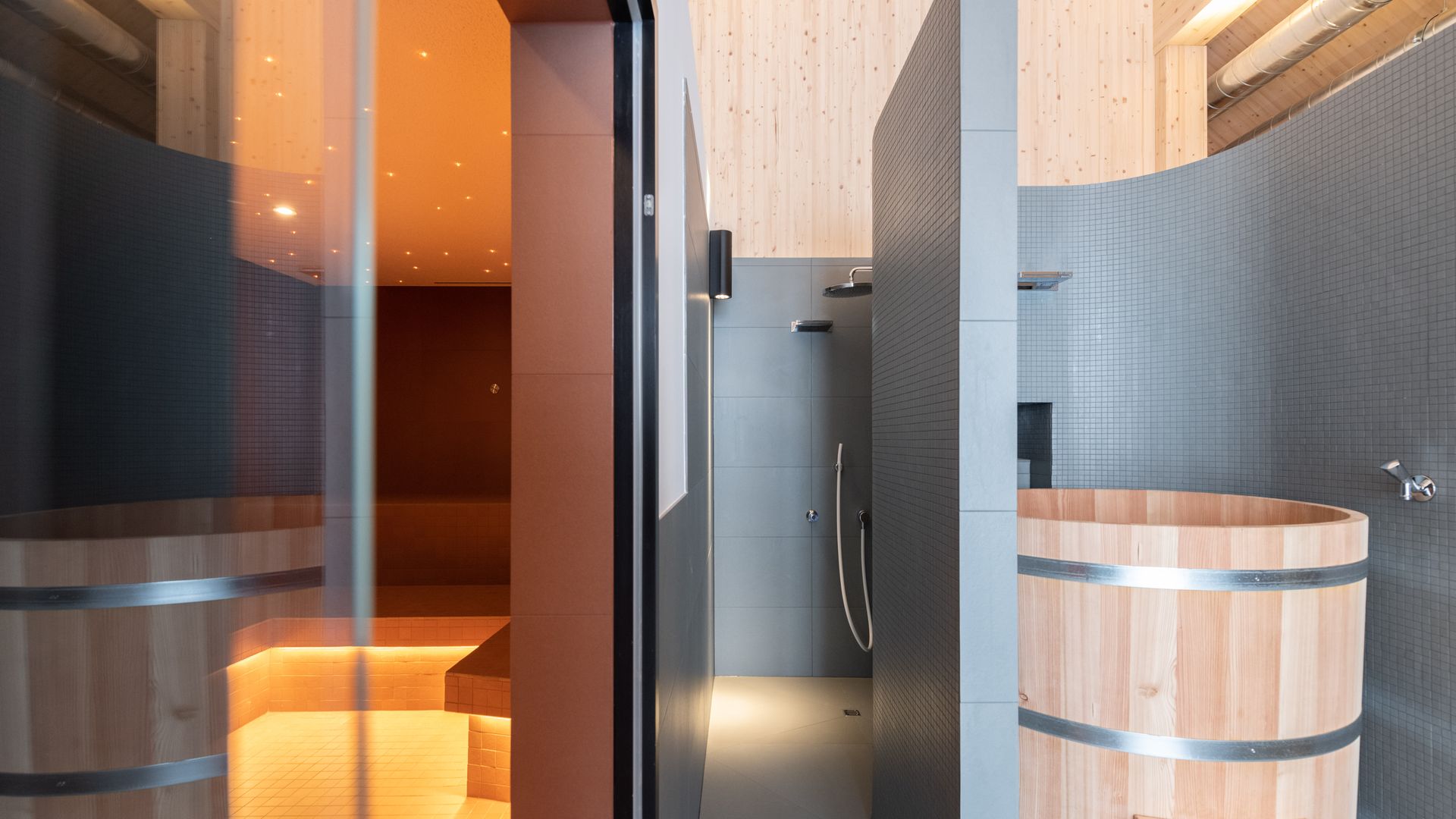 Moderner Spa-Innenbereich mit Saunen, Holzfass und stilvoller Beleuchtung.