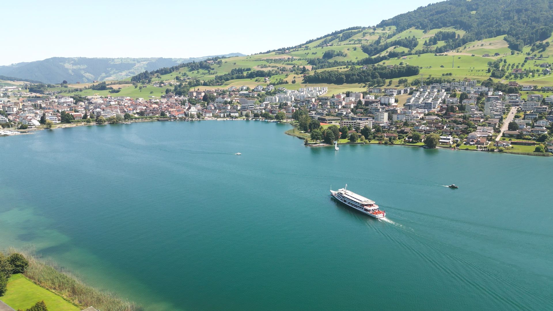 Motor vessel cruising on Küssnacht Lake with town and green hills in the background.