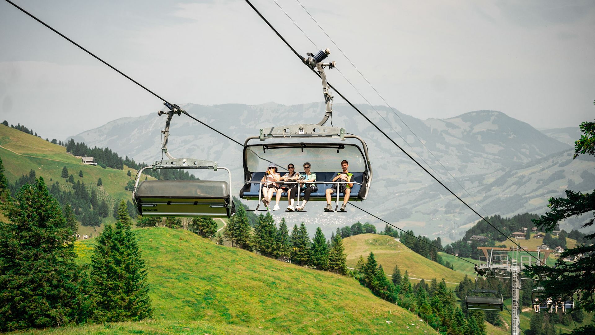 Sesselbahn am Klingenstock mit Fahrgästen über grünen Hängen und Berglandschaft.