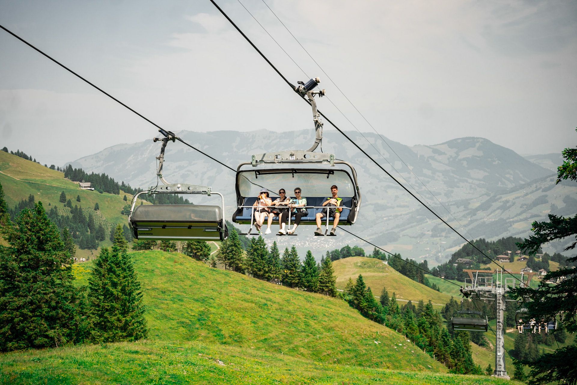 Chairlift at Klingenstock with passengers above green slopes and mountain landscape.