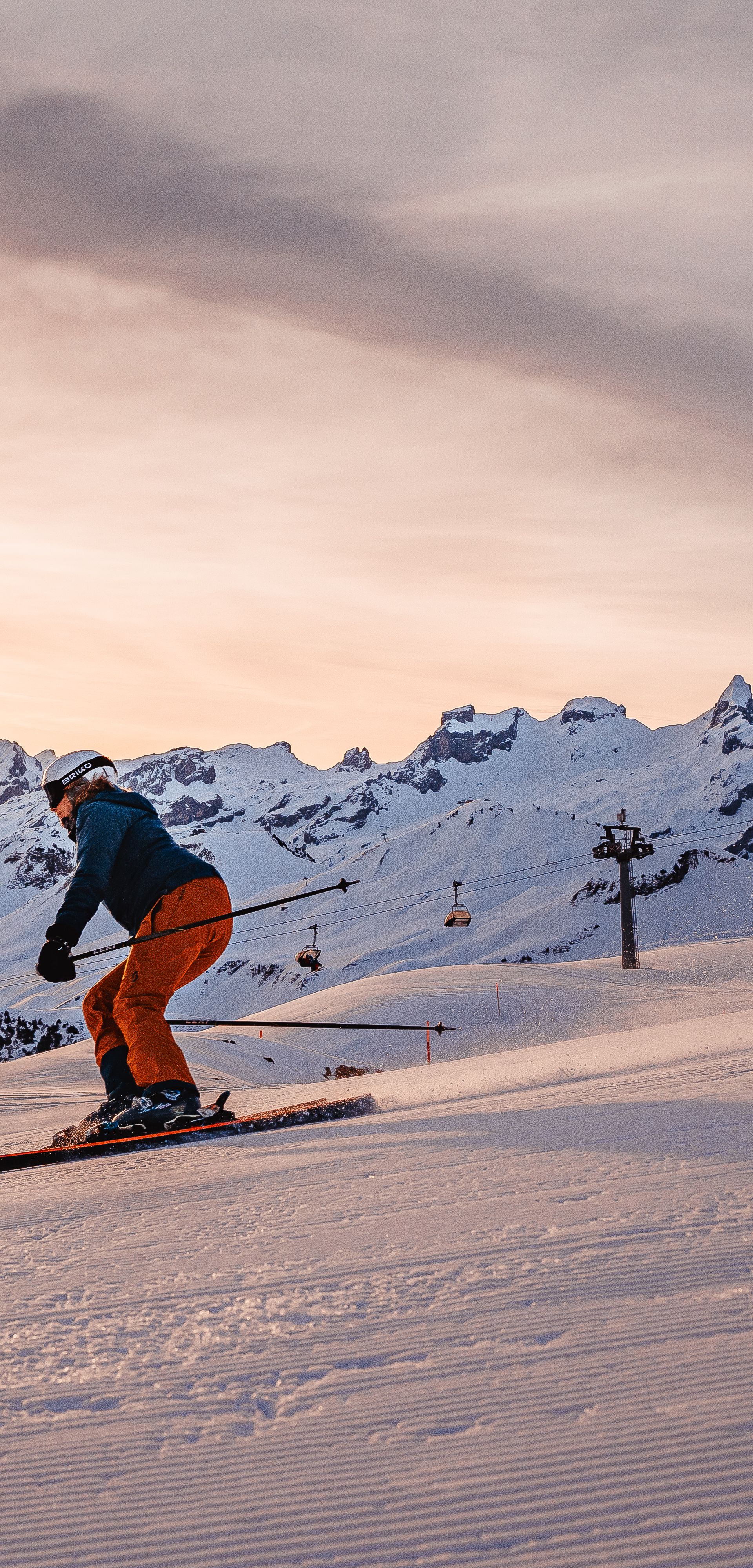 Skifahrer auf einer präparierten Piste bei Sonnenaufgang, mit verschneiter Berglandschaft im Hintergrund.