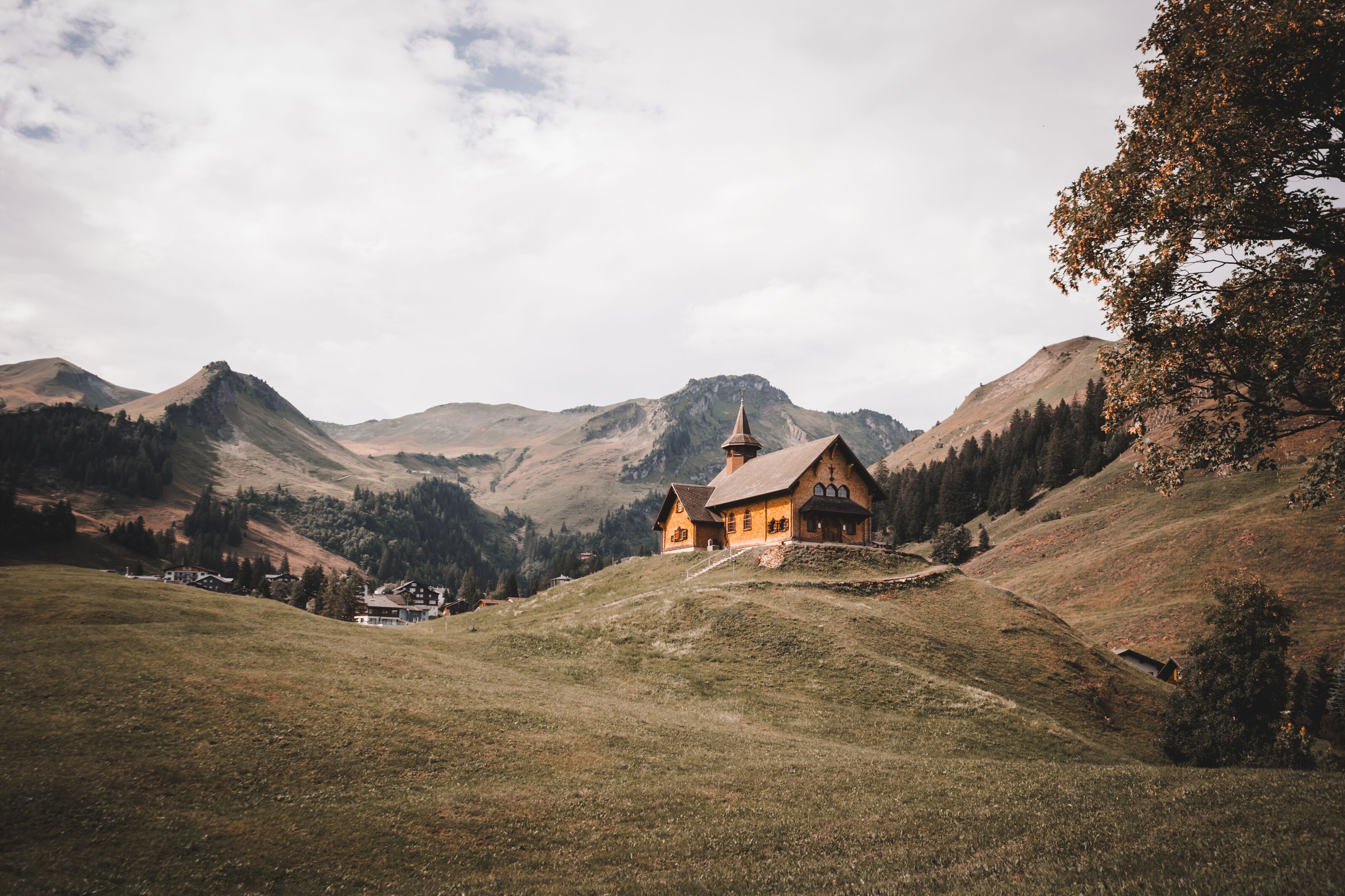 Kapelle auf einem Hügel in alpiner Landschaft, umgeben von Wiesen und Bergen.