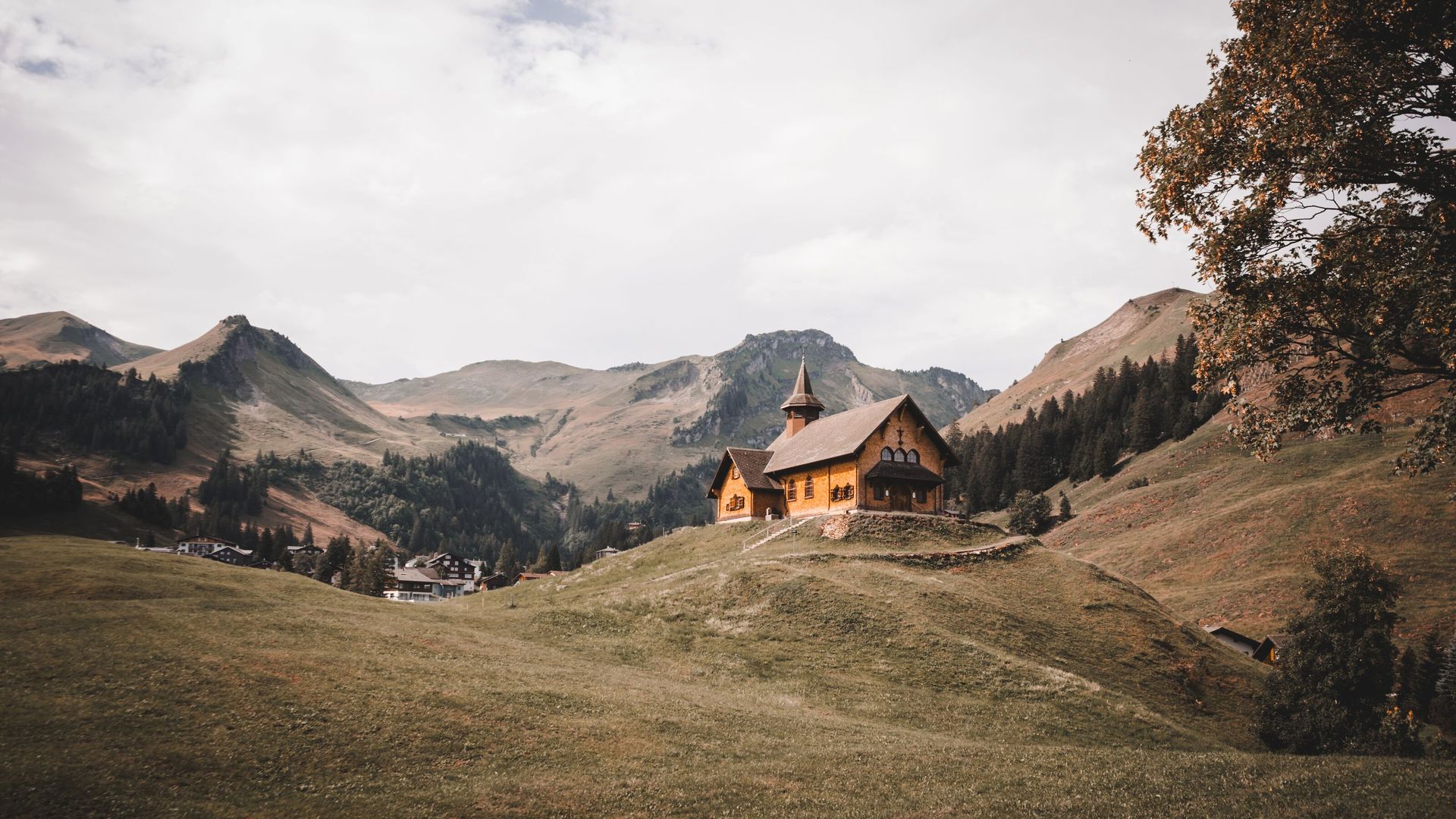 Kapelle auf einem Hügel in alpiner Landschaft, umgeben von Wiesen und Bergen.