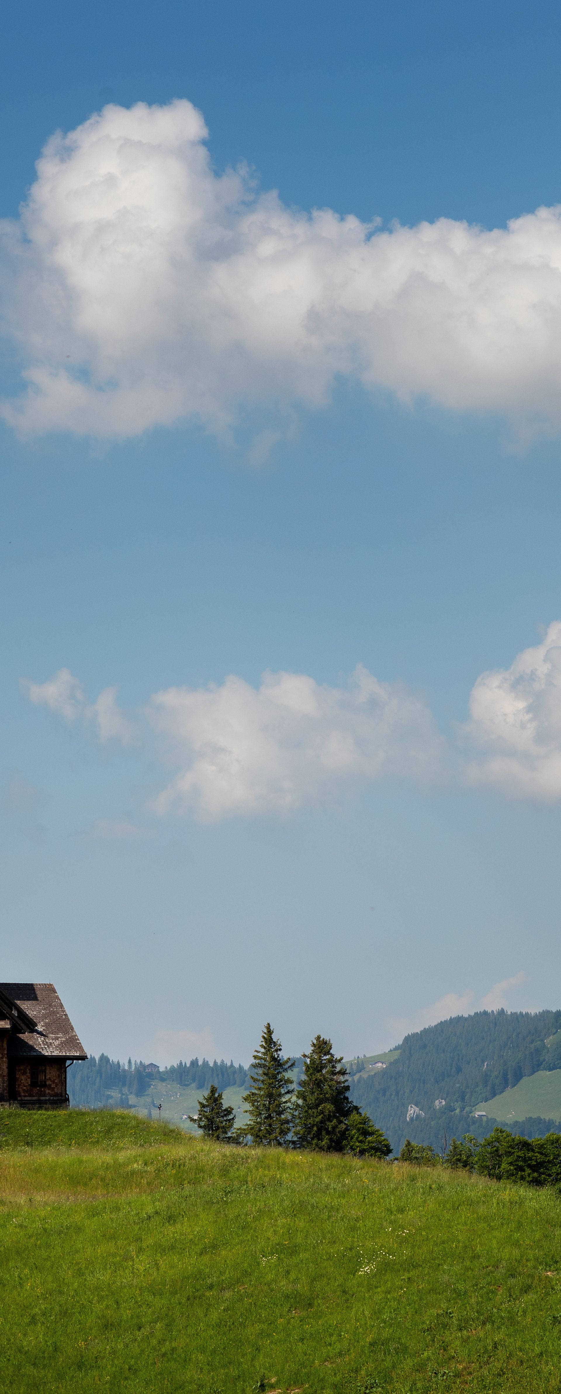 Kapelle auf einem grünen Hügel mit Blick auf markante Berggipfel und blauen Himmel.