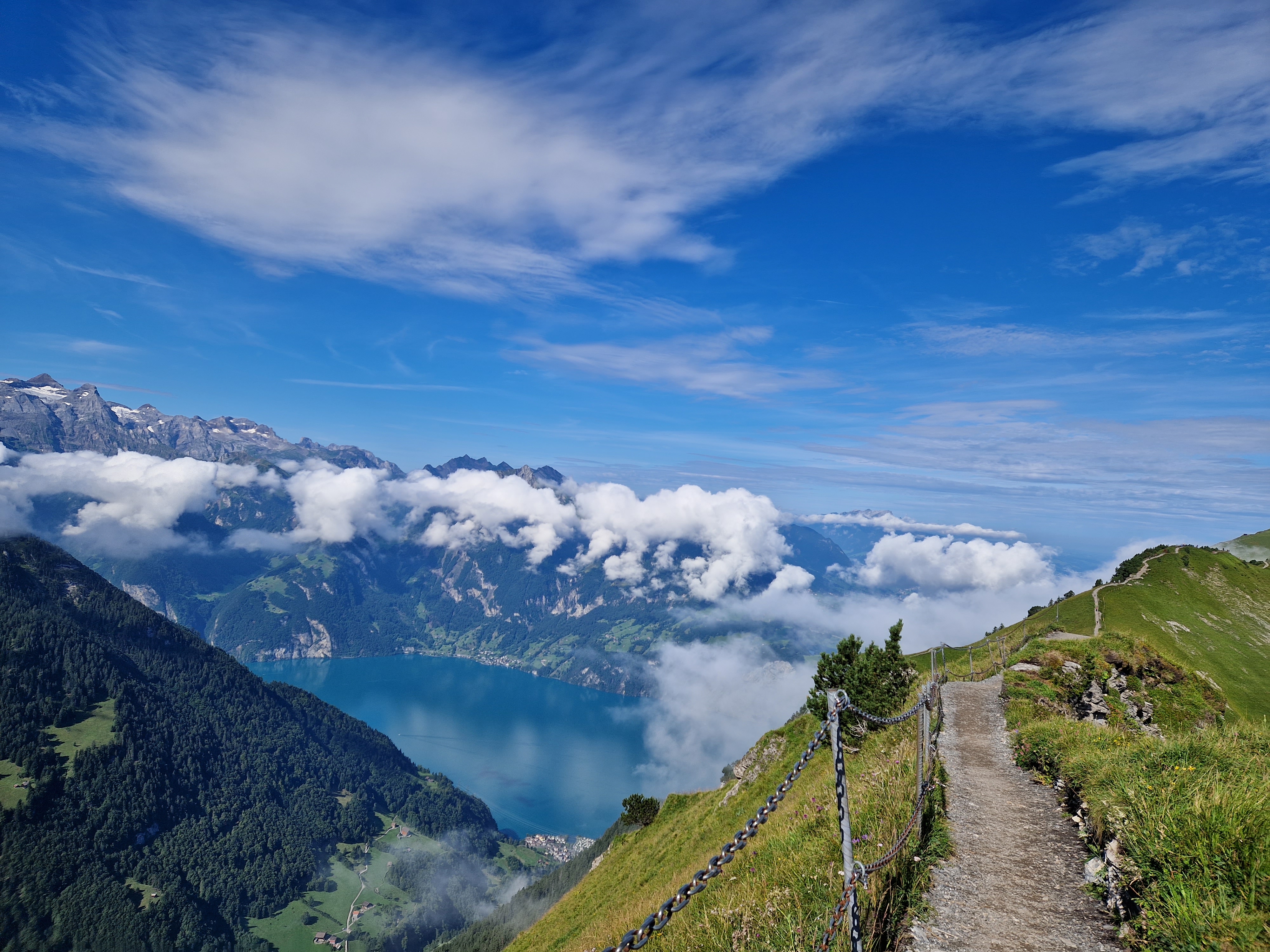 Mountain ridge trail overlooking Lake Lucerne, surrounded by clouds and alpine landscape.