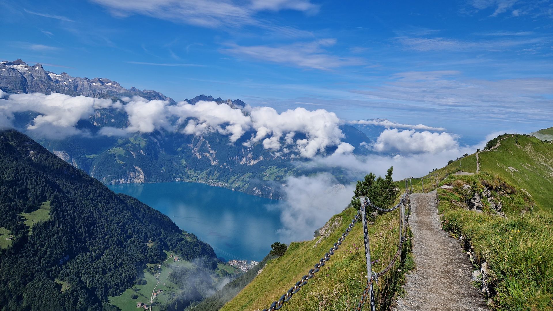 Bergwanderweg am Grat mit Blick auf den Vierwaldstättersee, umgeben von Wolken und alpiner Landschaft.