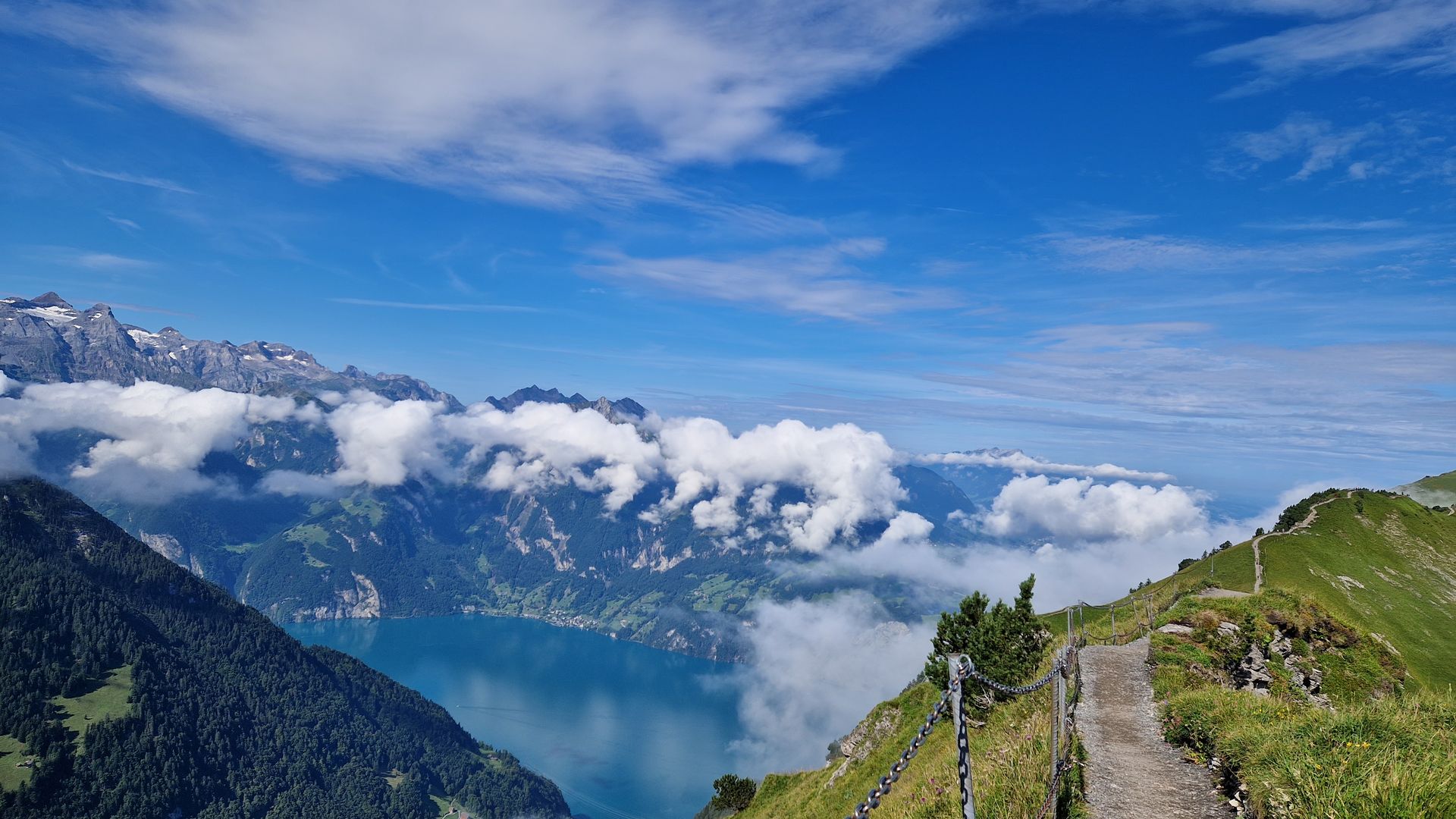 Mountain ridge trail overlooking Lake Lucerne, surrounded by clouds and alpine landscape.