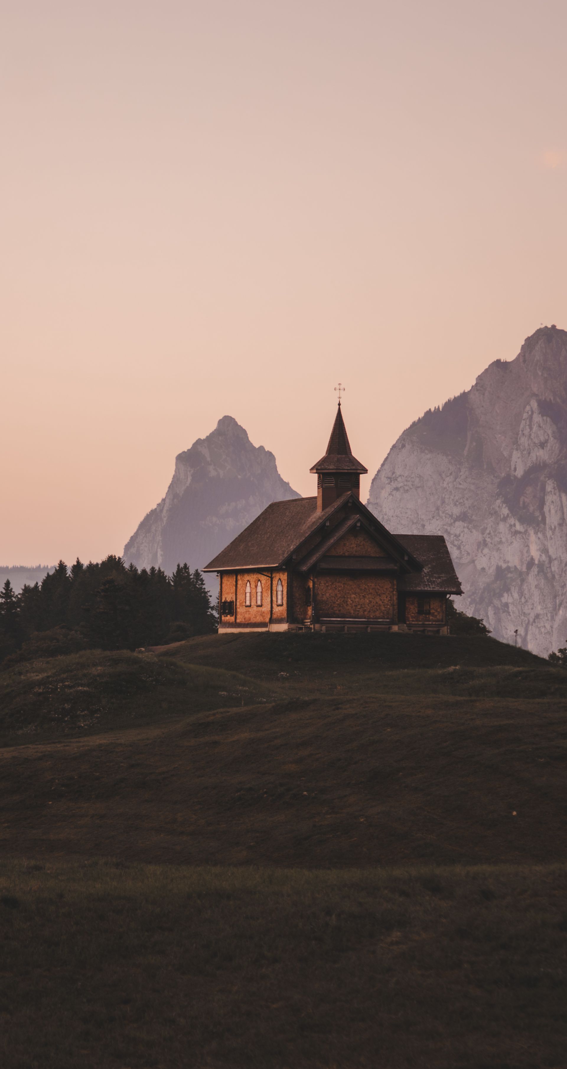 Kapelle auf einem Hügel im Abendlicht mit Berggipfeln im Hintergrund.