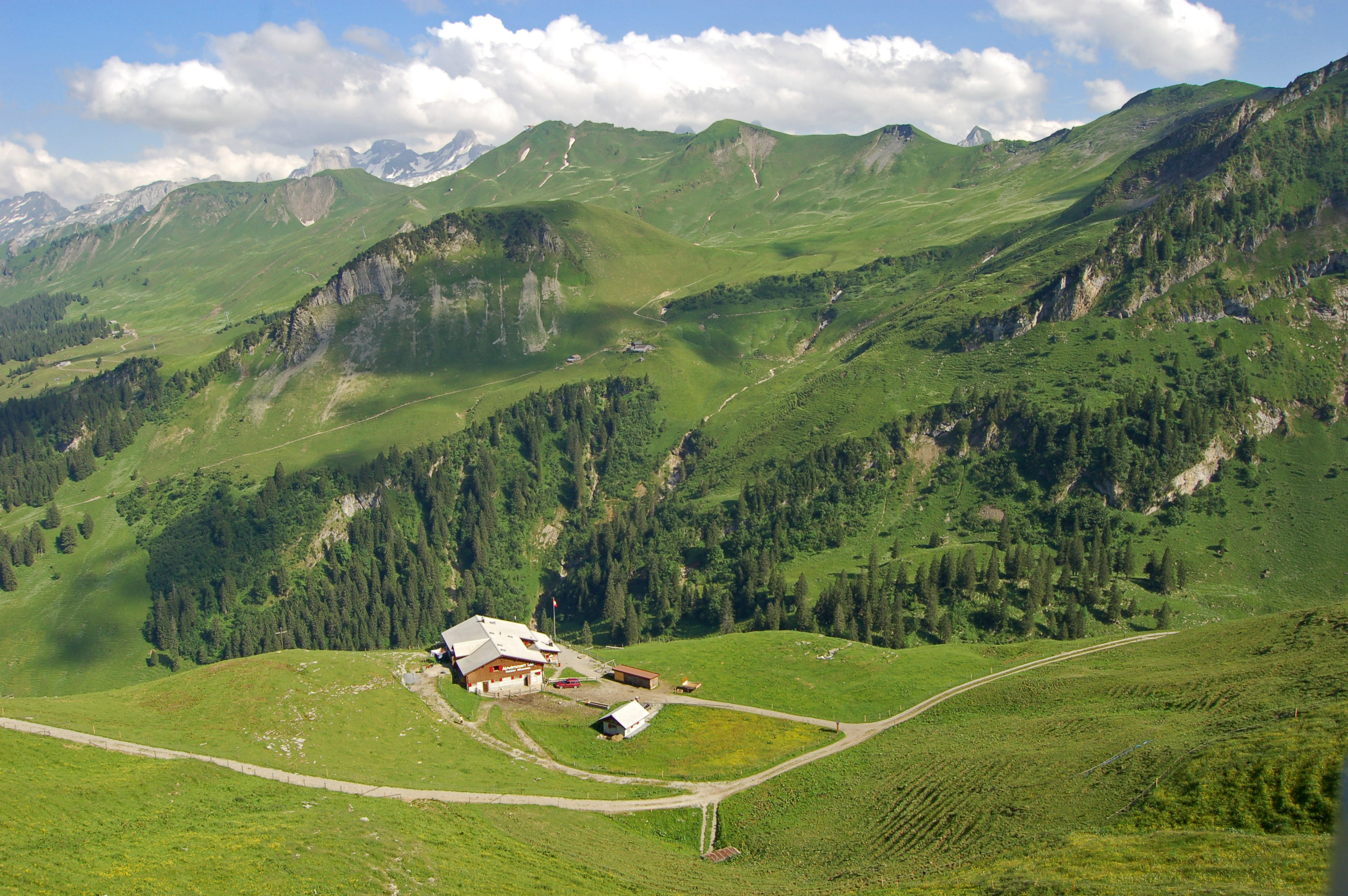 Bergrestaurant inmitten einer weiten grünen Berglandschaft mit Blick auf die umliegenden Hügel.