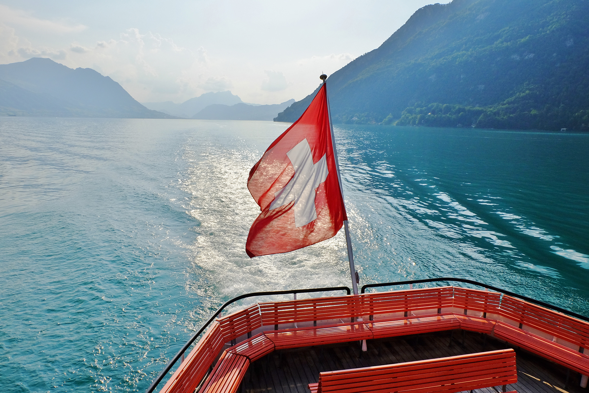 Stern of a vessel with Swiss flag on Lake Lucerne surrounded by the mountains of Central Switzerland