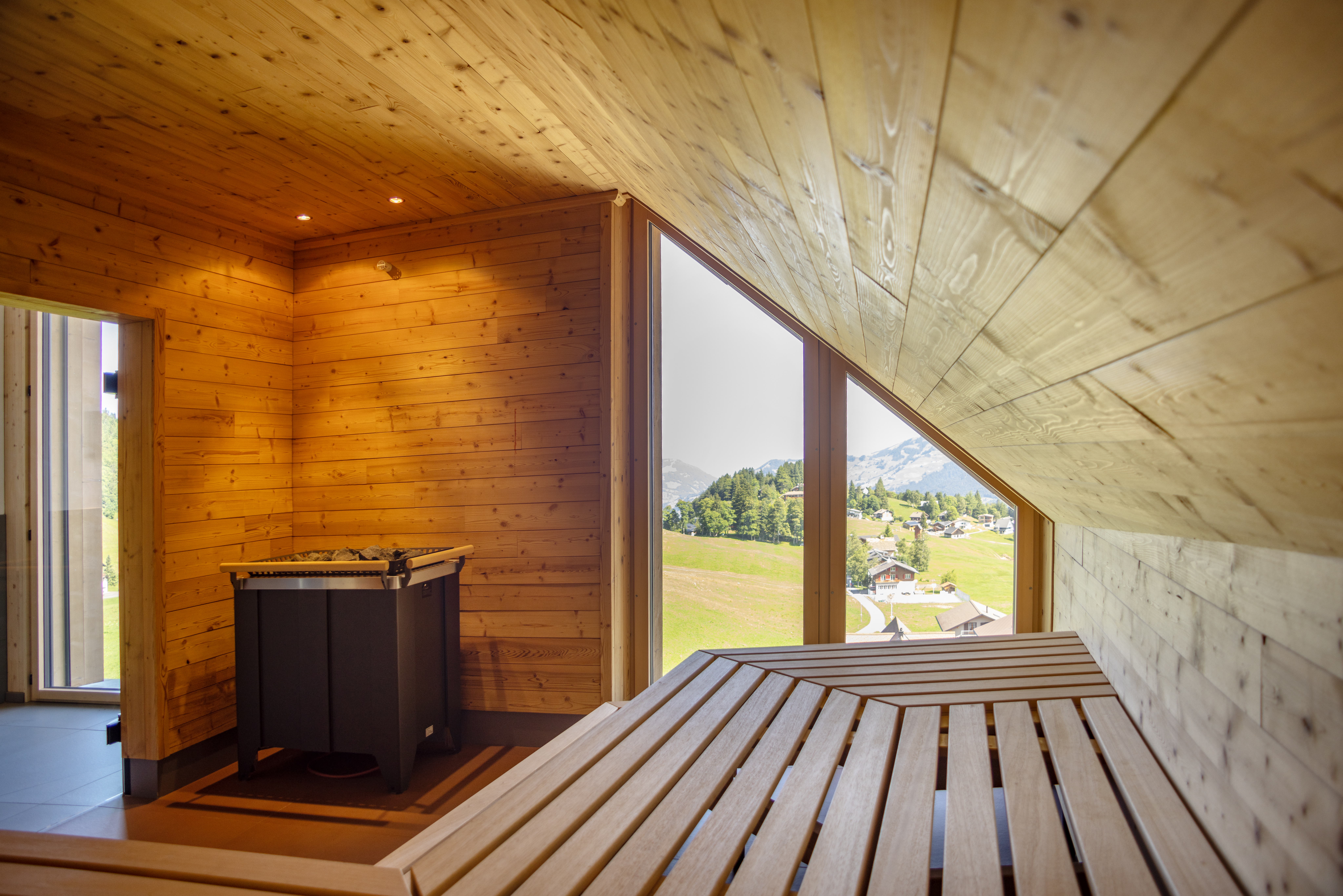 Saunaraum aus Holz mit Liegeflächen und grossem Fenster mit Blick in die Natur.
