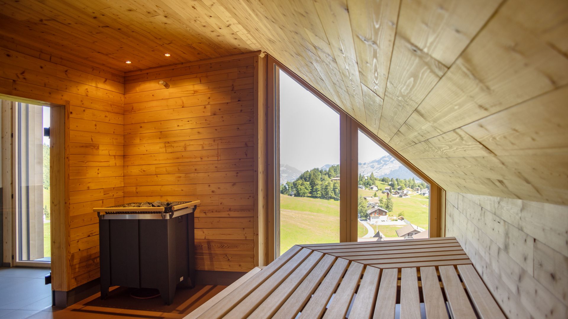 Saunaraum aus Holz mit Liegeflächen und grossem Fenster mit Blick in die Natur.