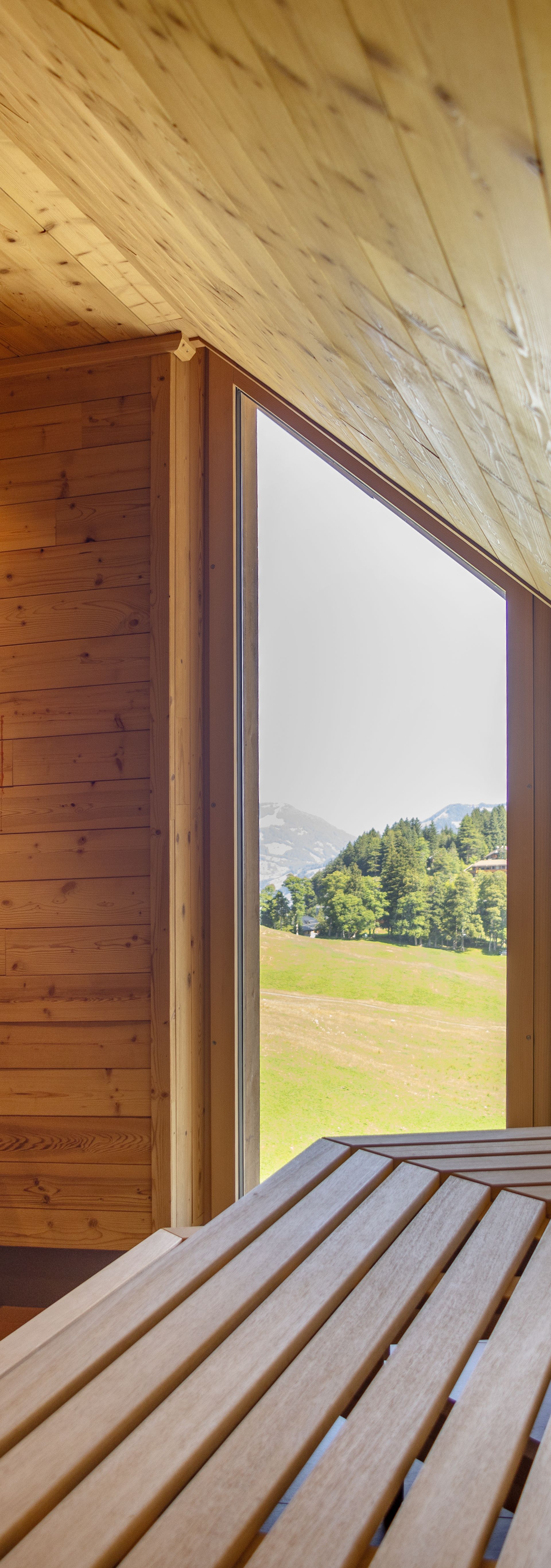 Saunaraum aus Holz mit Liegeflächen und grossem Fenster mit Blick in die Natur.