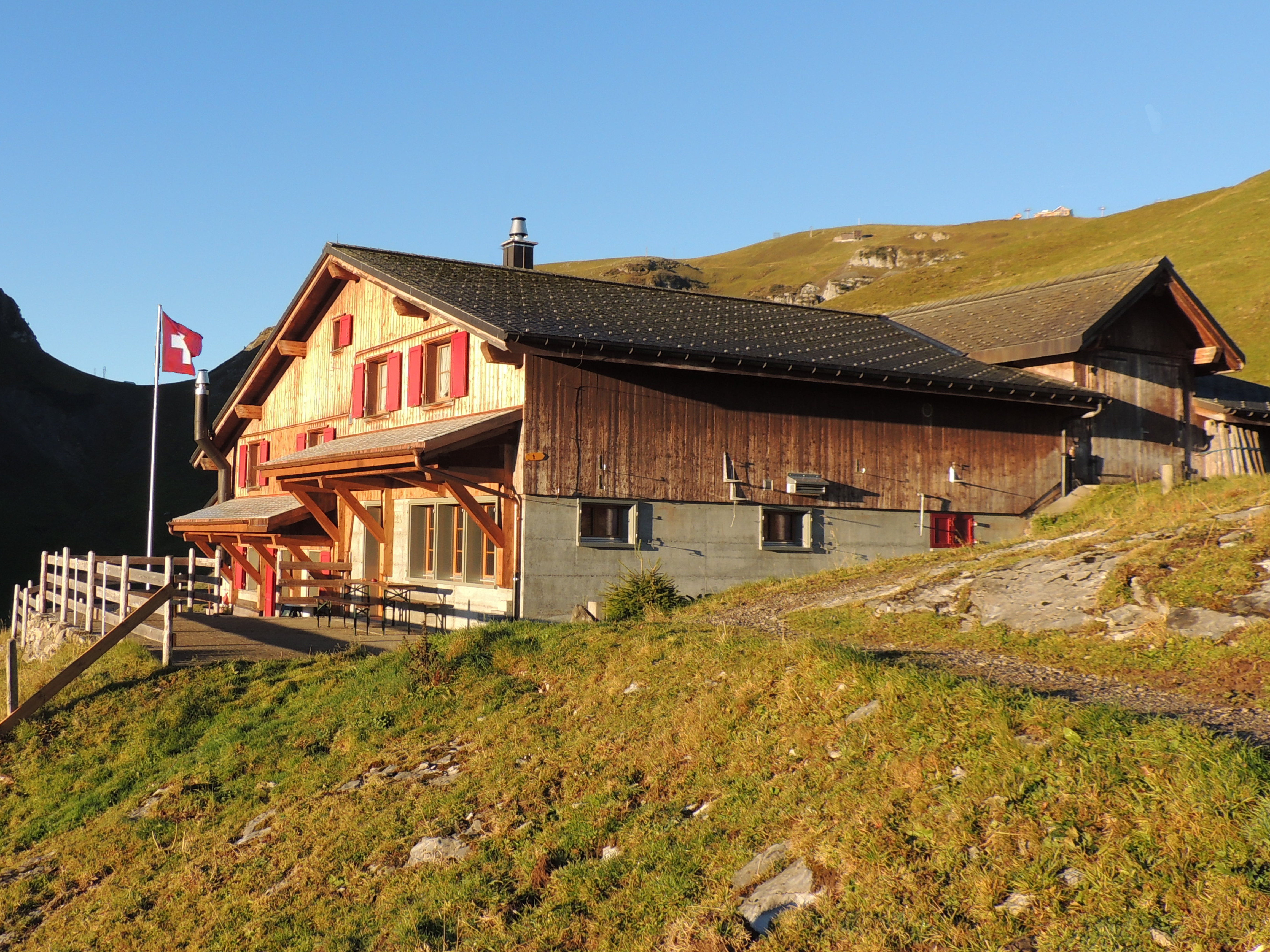 Bergrestaurant auf einem Hügel im Sonnenlicht mit Terrasse und Blick auf die alpine Landschaft.