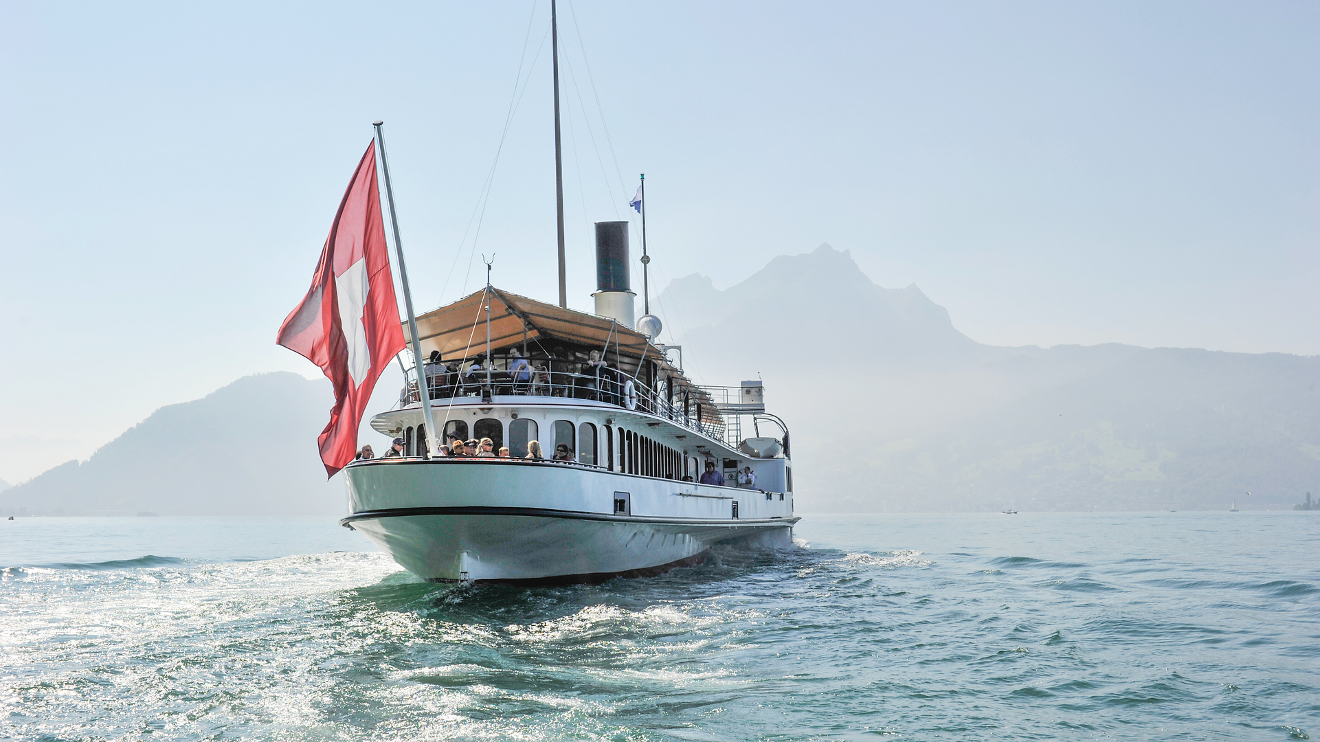 Historischer Dampfer mit Schweizer Flagge auf dem Vierwaldstättersee vor Bergkulisse.