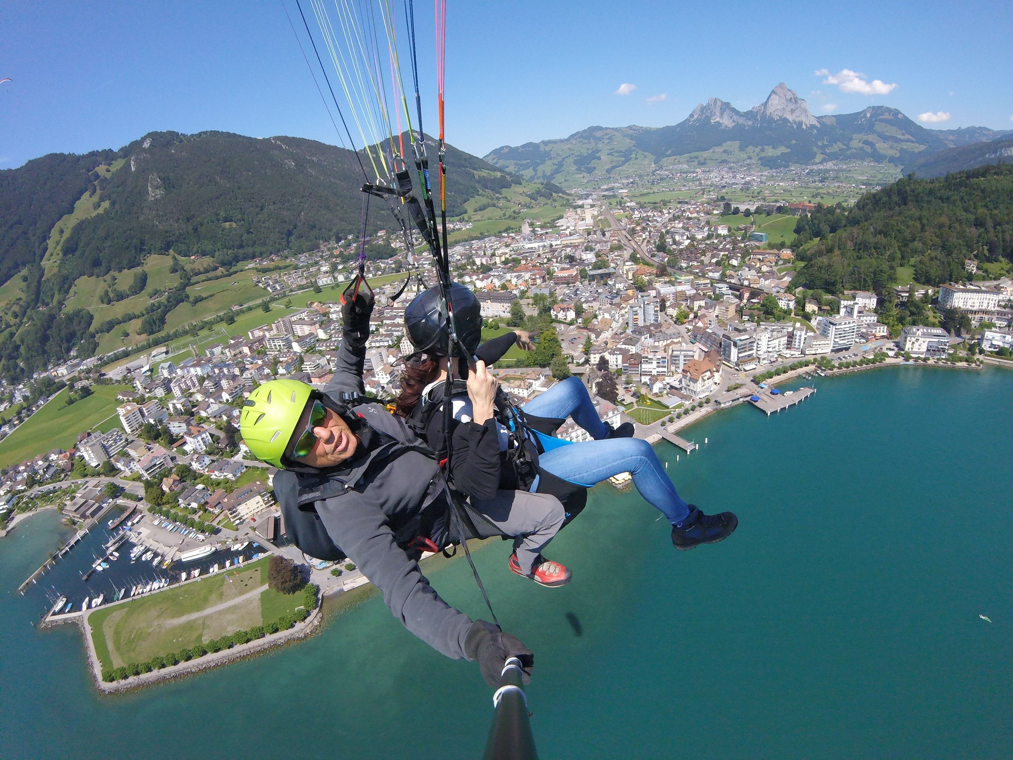 Zwei Personen beim Tandem-Paragliding über dem Vierwaldstättersee mit Blick auf Berge und Landschaft.