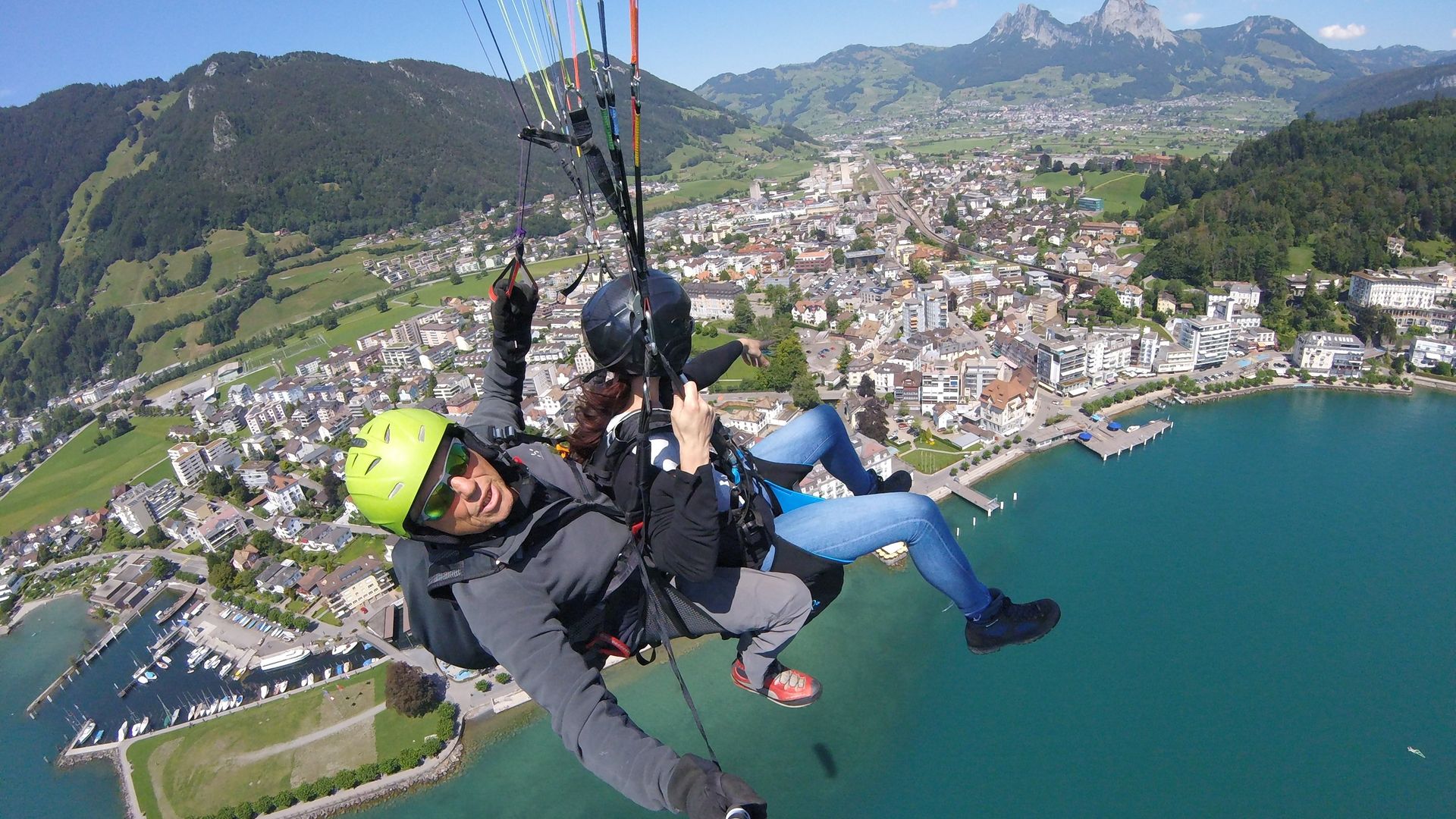 Zwei Personen beim Tandem-Paragliding über dem Vierwaldstättersee mit Blick auf Berge und Landschaft.