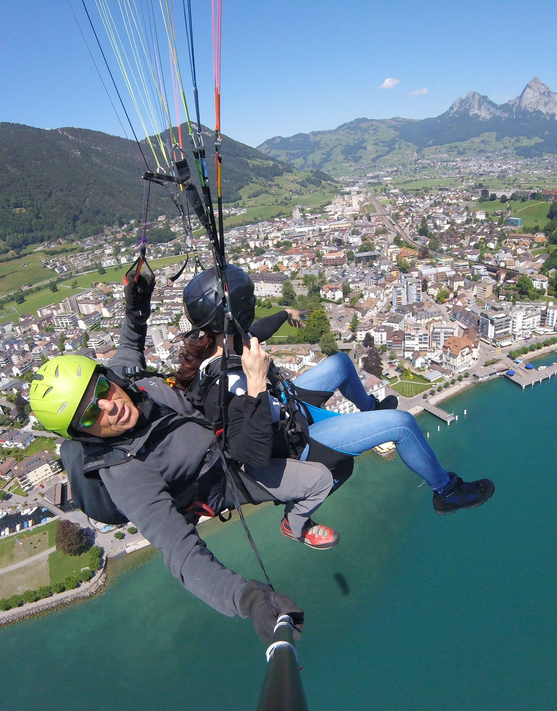Zwei Personen beim Tandem-Paragliding über dem Vierwaldstättersee mit Blick auf Berge und Landschaft.