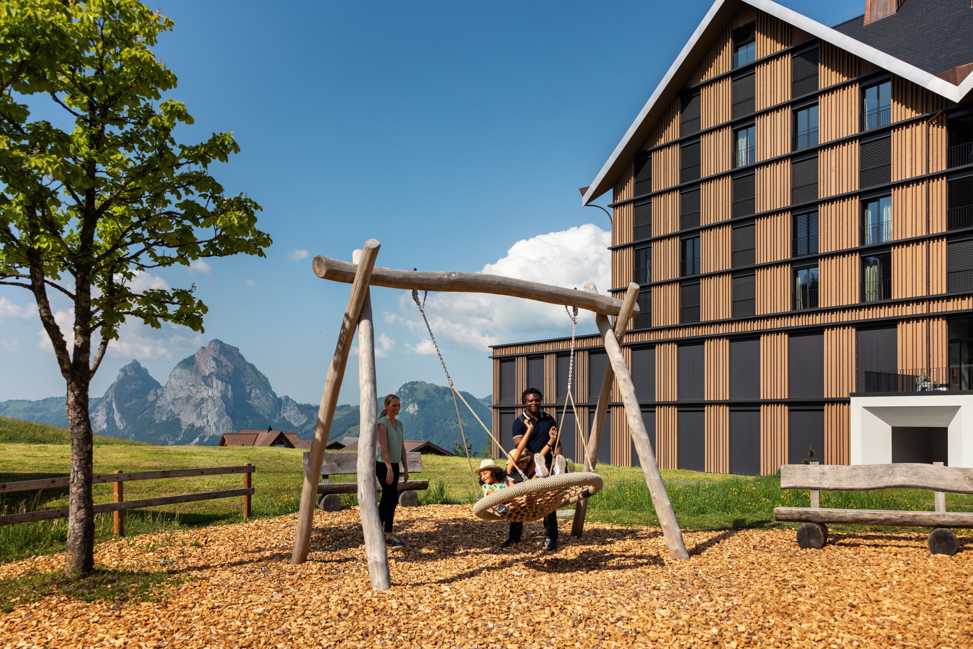 Swing on a playground next to a building with views of the alpine landscape.