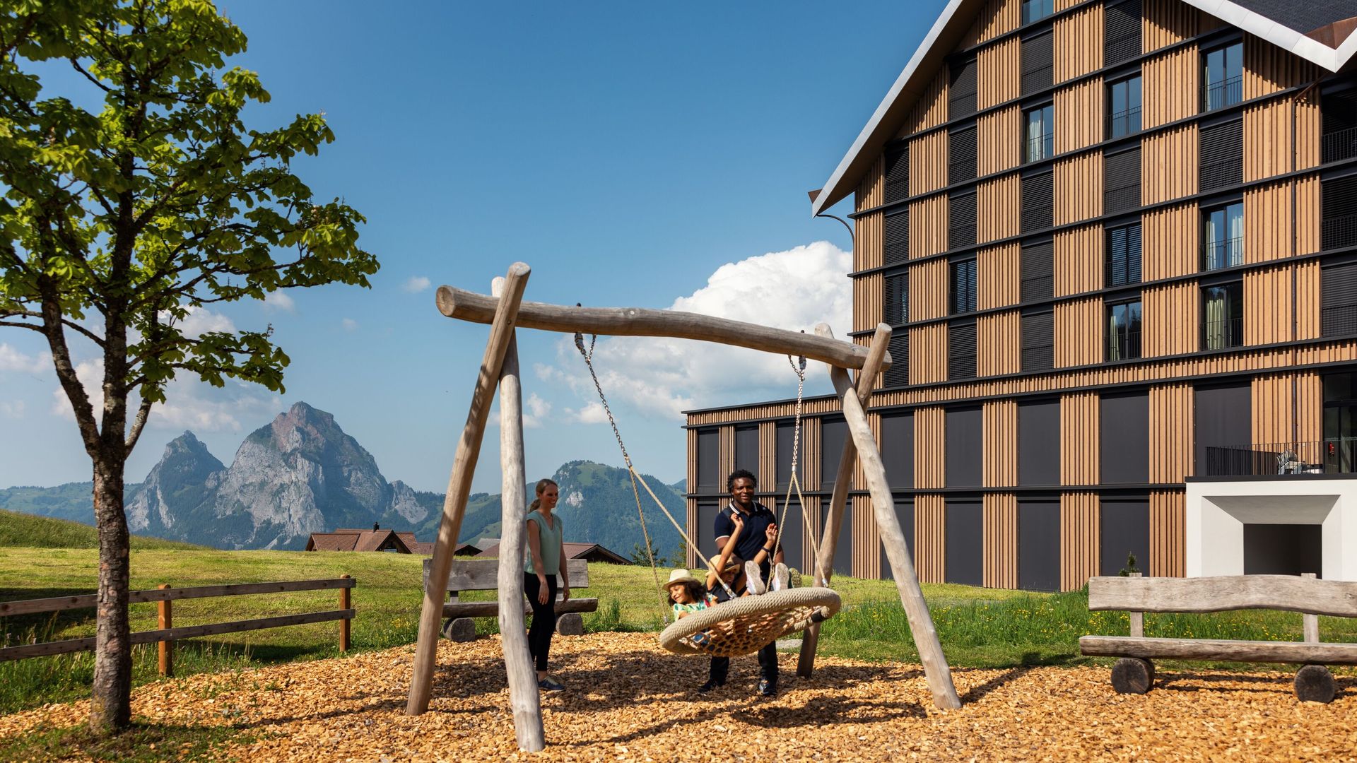 Swing on a playground next to a building with views of the alpine landscape.