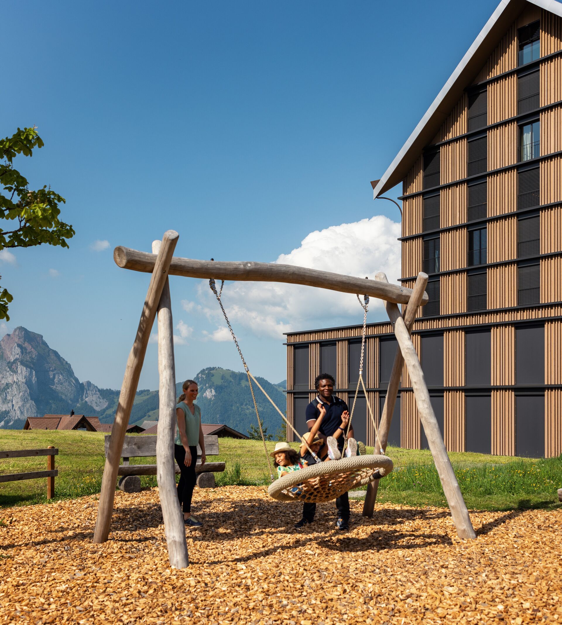 Schaukel auf einem Spielplatz neben einem Gebäude mit Blick auf die alpine Landschaft.