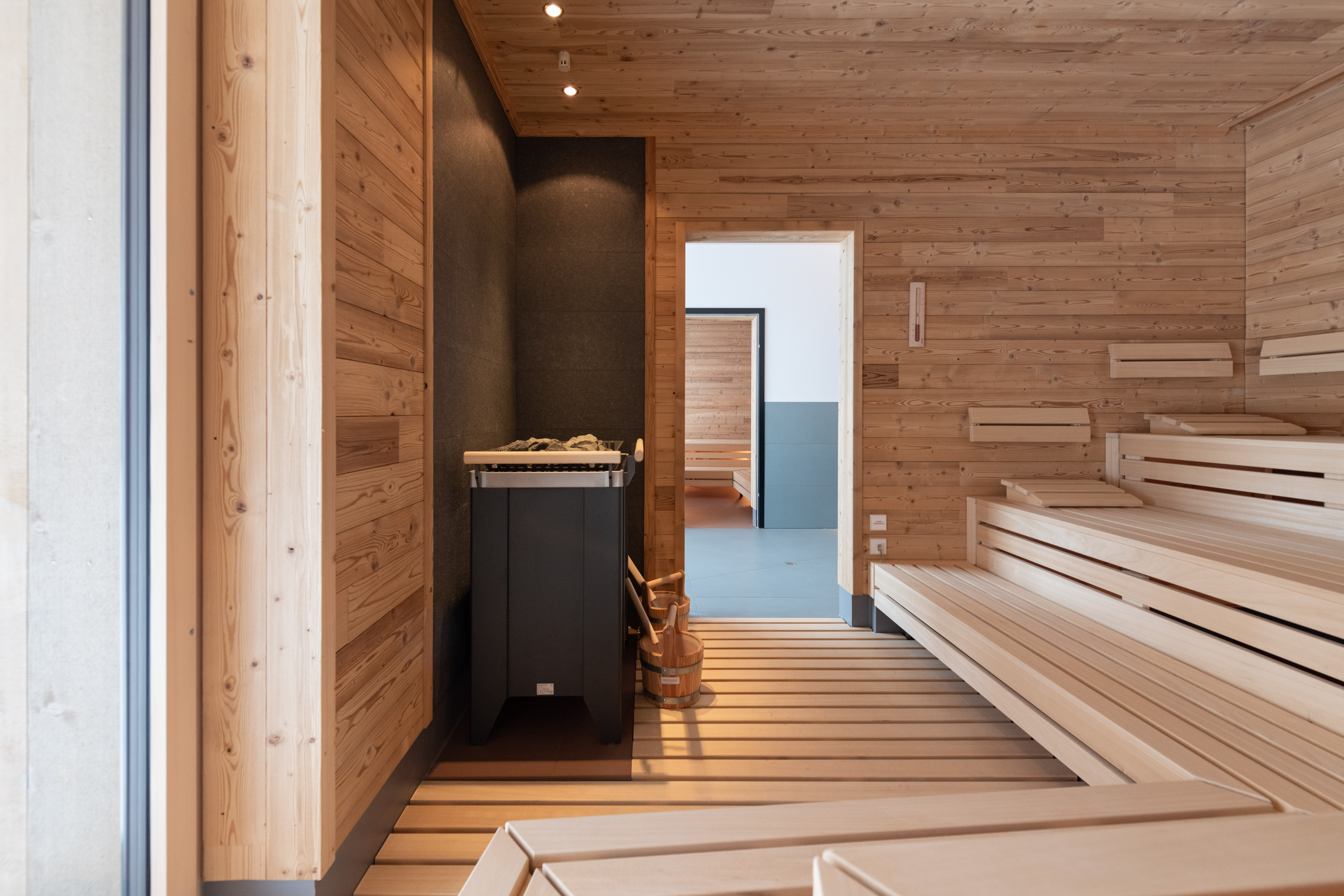 Heller Saunaraum aus Holz mit gestuften Sitzbänken und Ofen.