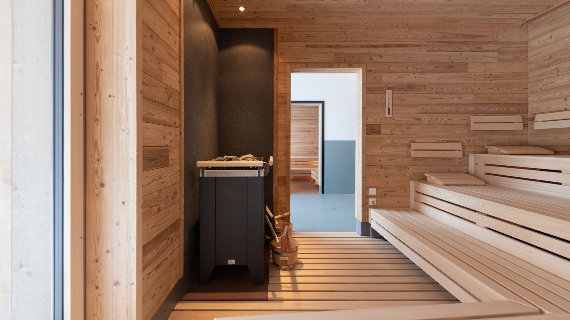 Heller Saunaraum aus Holz mit gestuften Sitzbänken und Ofen.