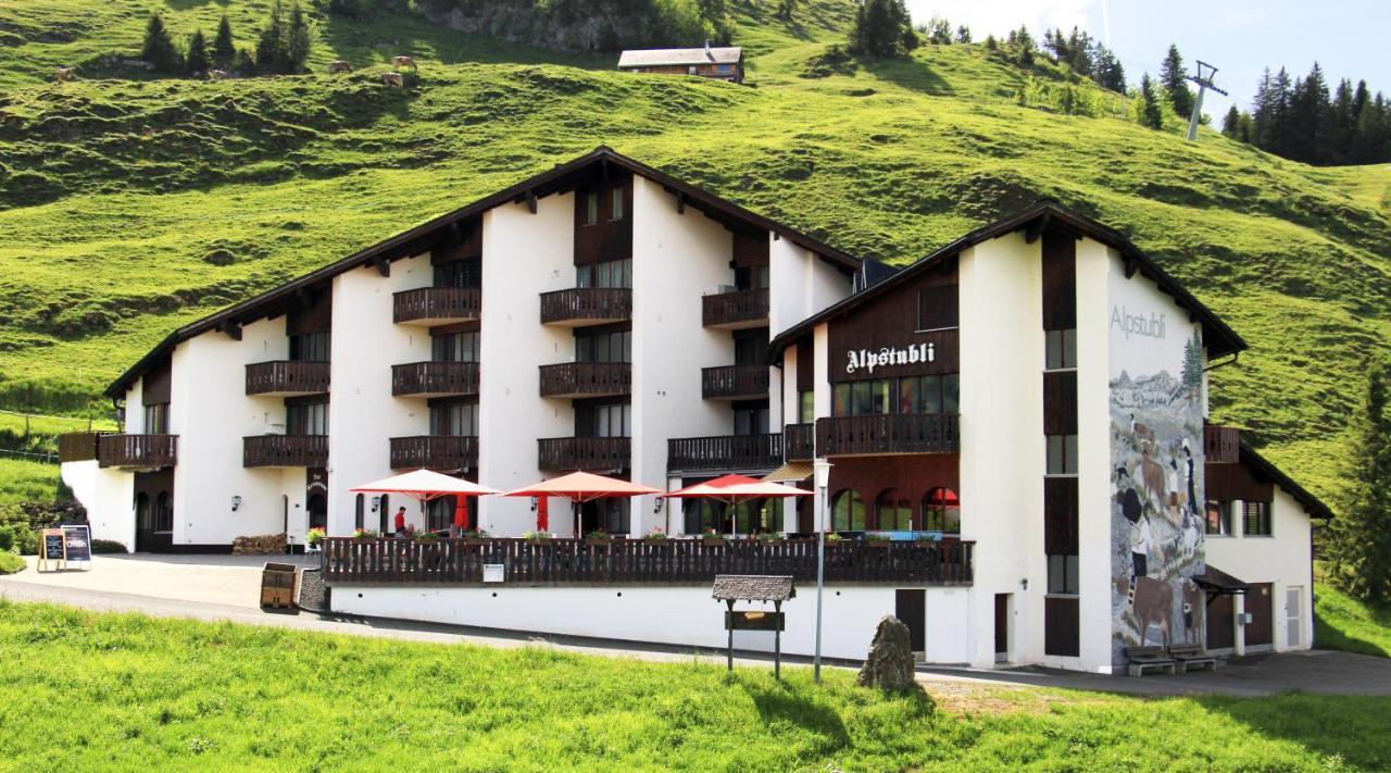 Bergrestaurant mit Terrasse auf einer Wiese in alpiner Landschaft.