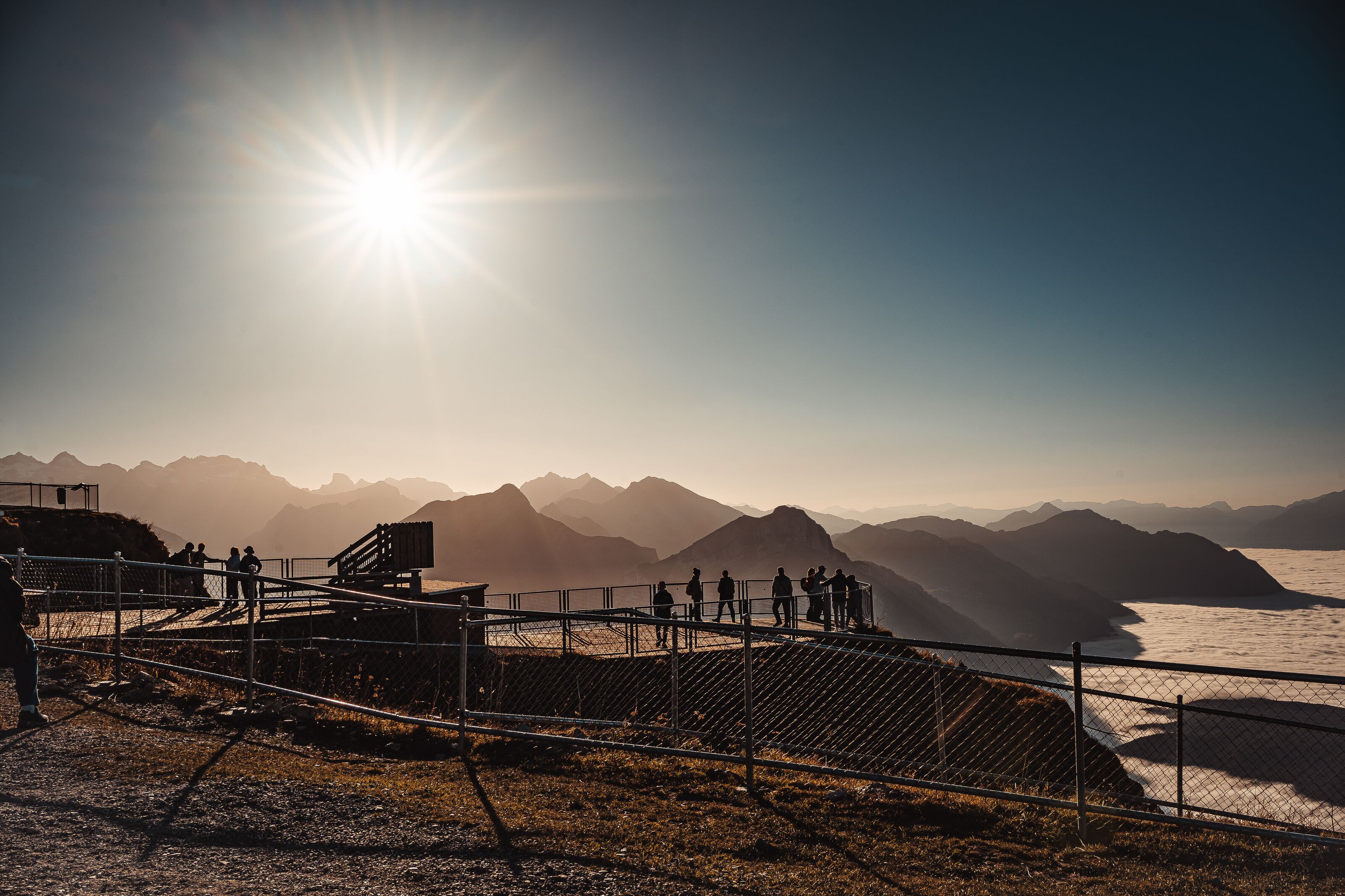 Viewing platform at Fronalpstock with visitors overlooking Lake Lucerne and the surrounding mountains in backlight.