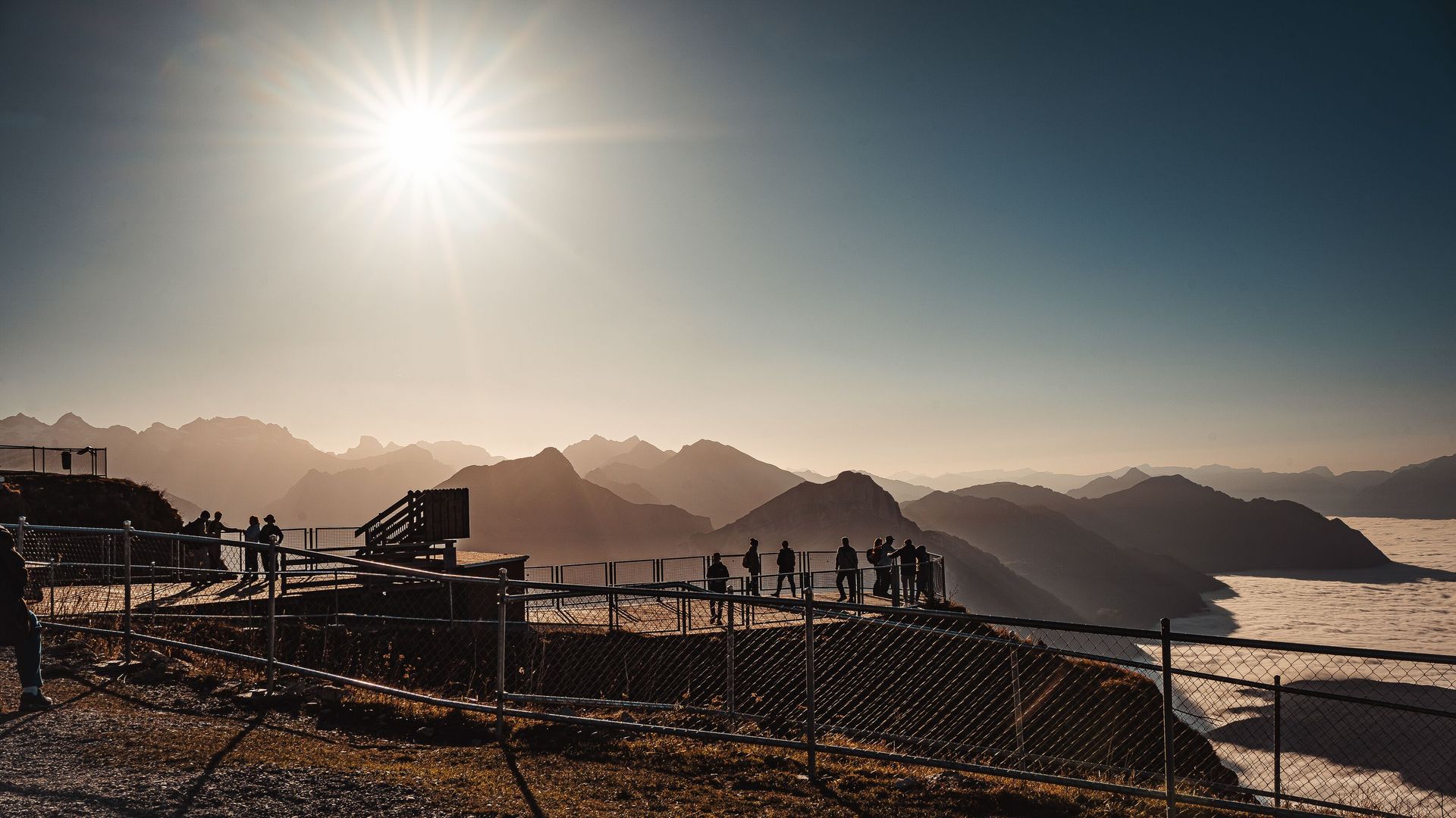 Viewing platform at Fronalpstock with visitors overlooking Lake Lucerne and the surrounding mountains in backlight.