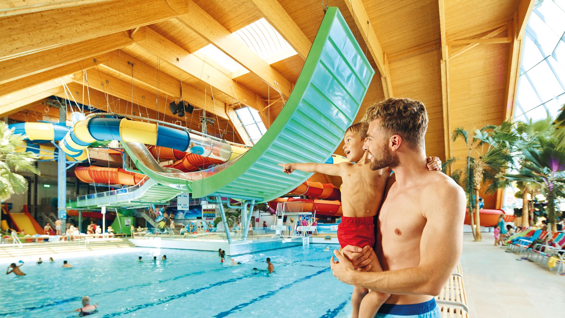 Vater hält seinen Sohn im Arm und blick auf das Schwimmbecken.