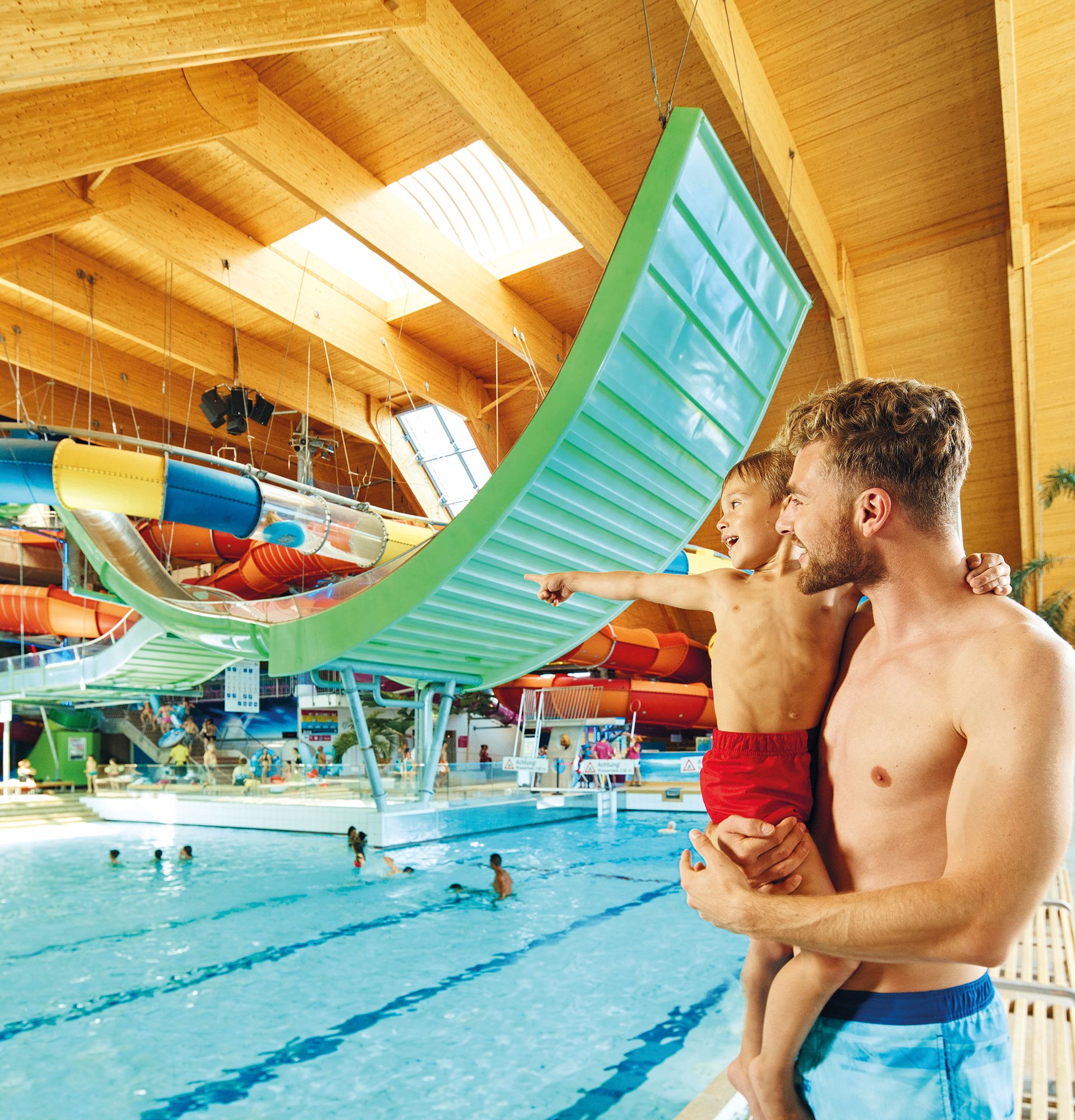 Vater hält seinen Sohn im Arm und blick auf das Schwimmbecken.