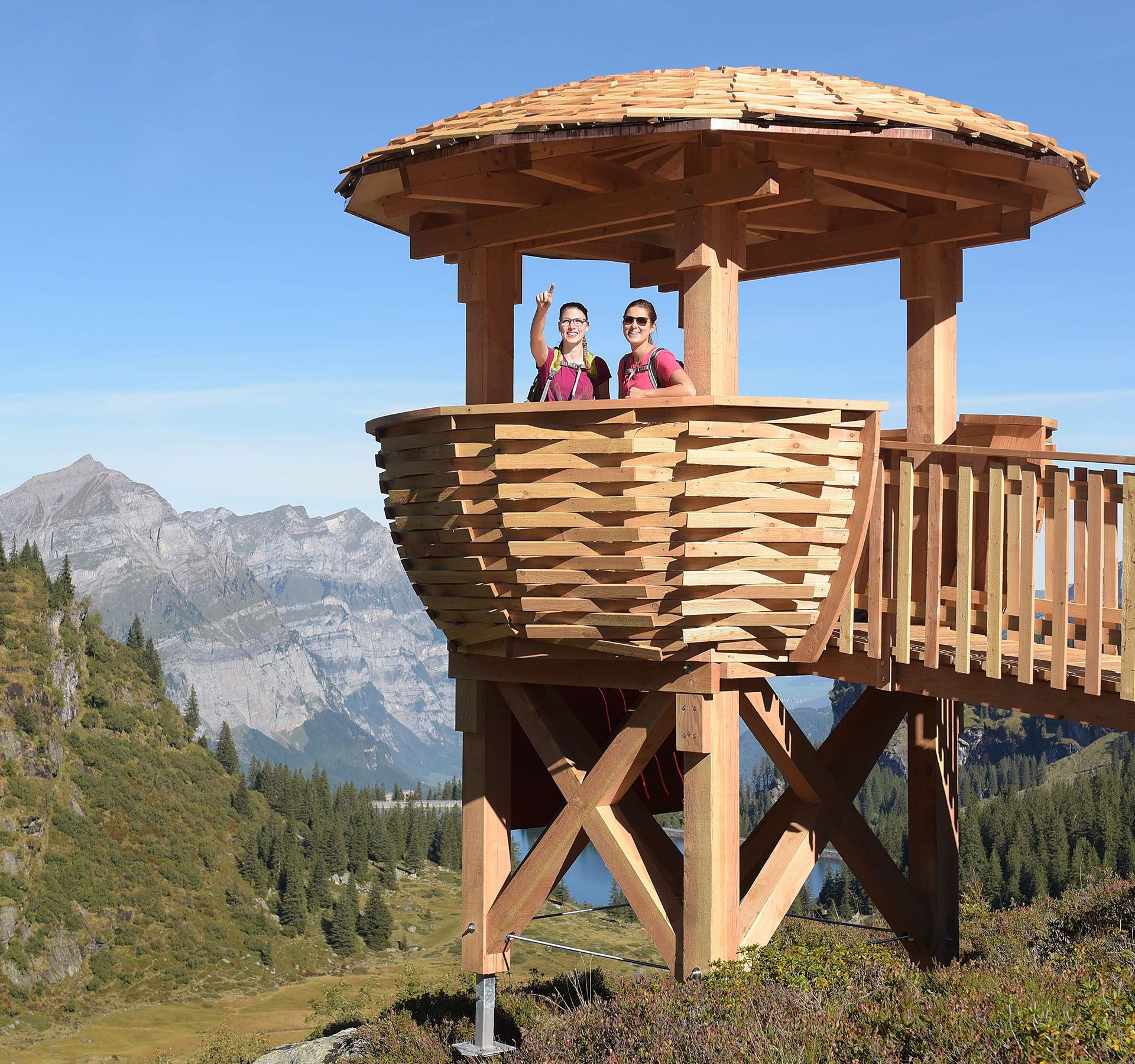 Deux femmes se tiennent sur une plate-forme panoramique en bois sur la Mettmenalp et discutent de leur itinéraire de randonnée.