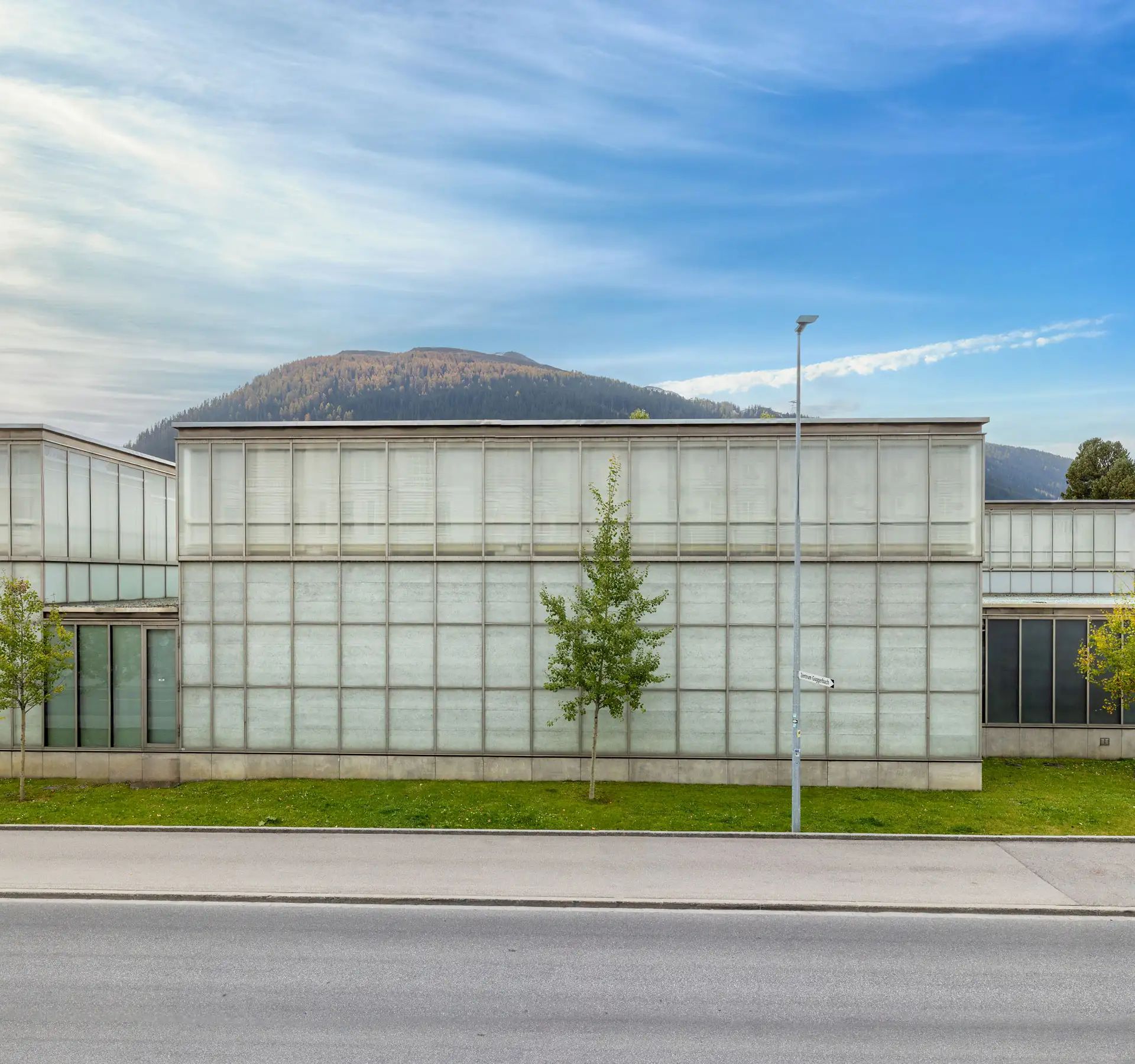 Das moderne Gebäude steht zwischen Bäumen, einer grünen Wiese und einem Berg im Hintergrund.