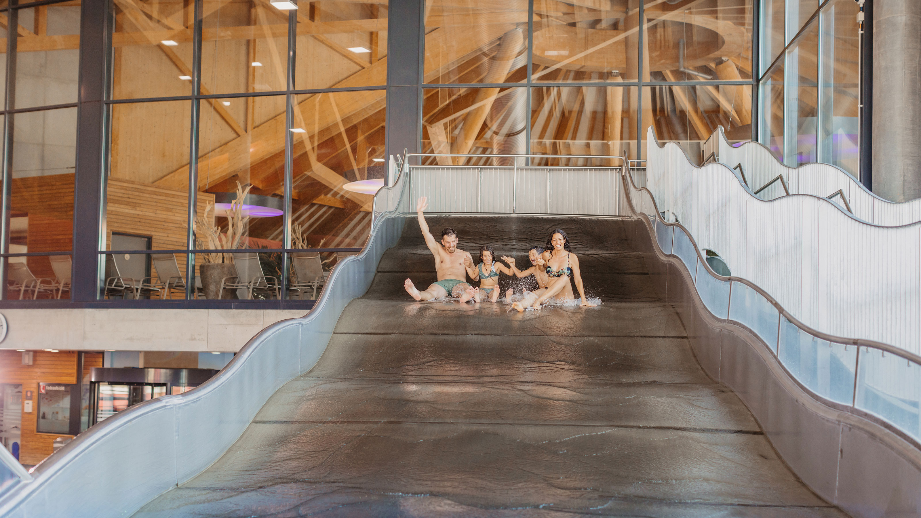 Two adults and two children sliding side by side on a wide water slide at Bad Aquabasilea