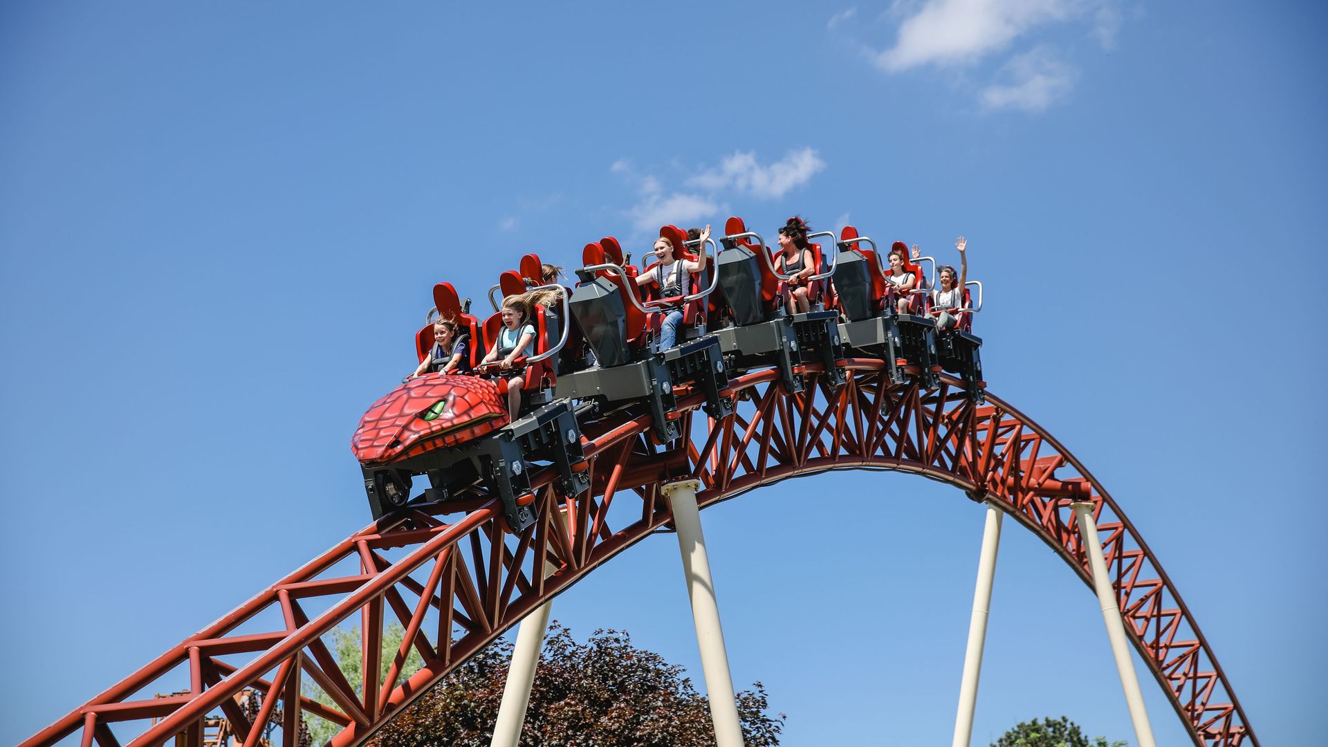 Eine rote Achterbahn mit Gästen, die ihre Hände in die Höhe strecken.