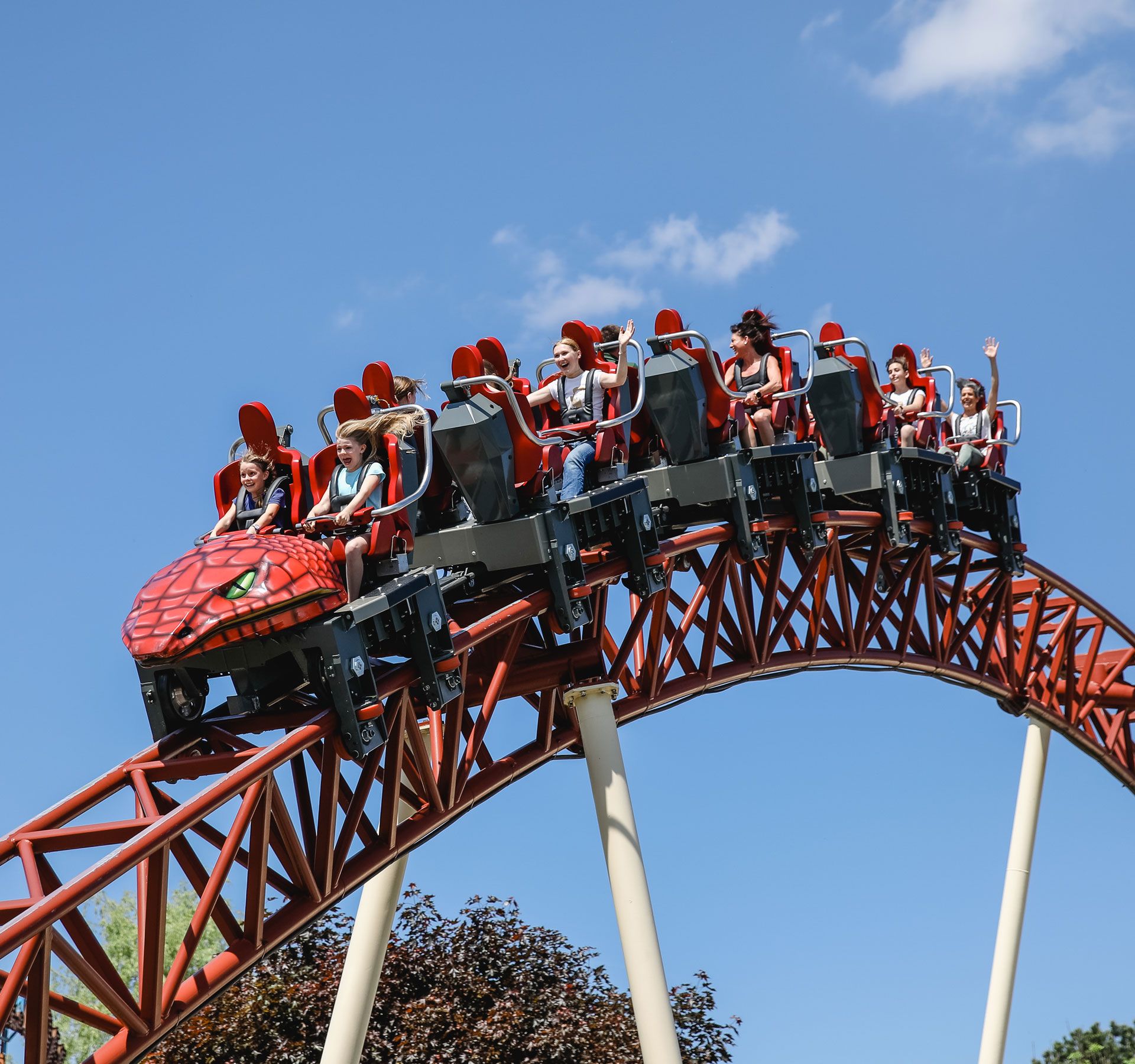 Eine rote Achterbahn mit Gästen, die ihre Hände in die Höhe strecken.
