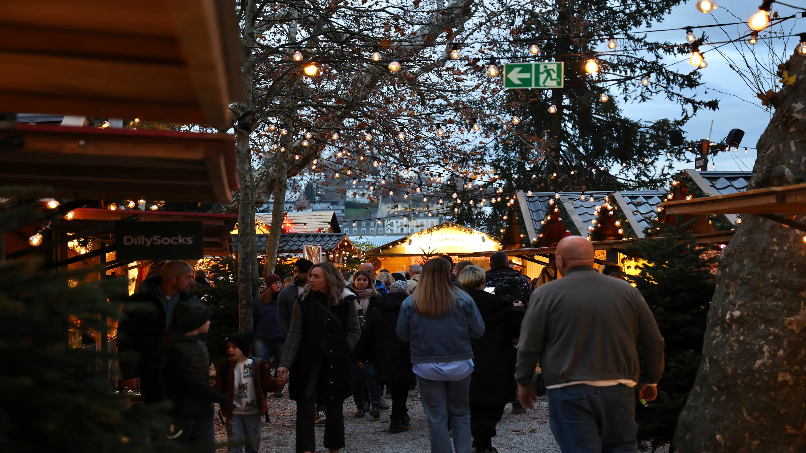 Des gens se promènent entre les stands en bois illuminés d'un marché de Noël, à la lueur du soir.
