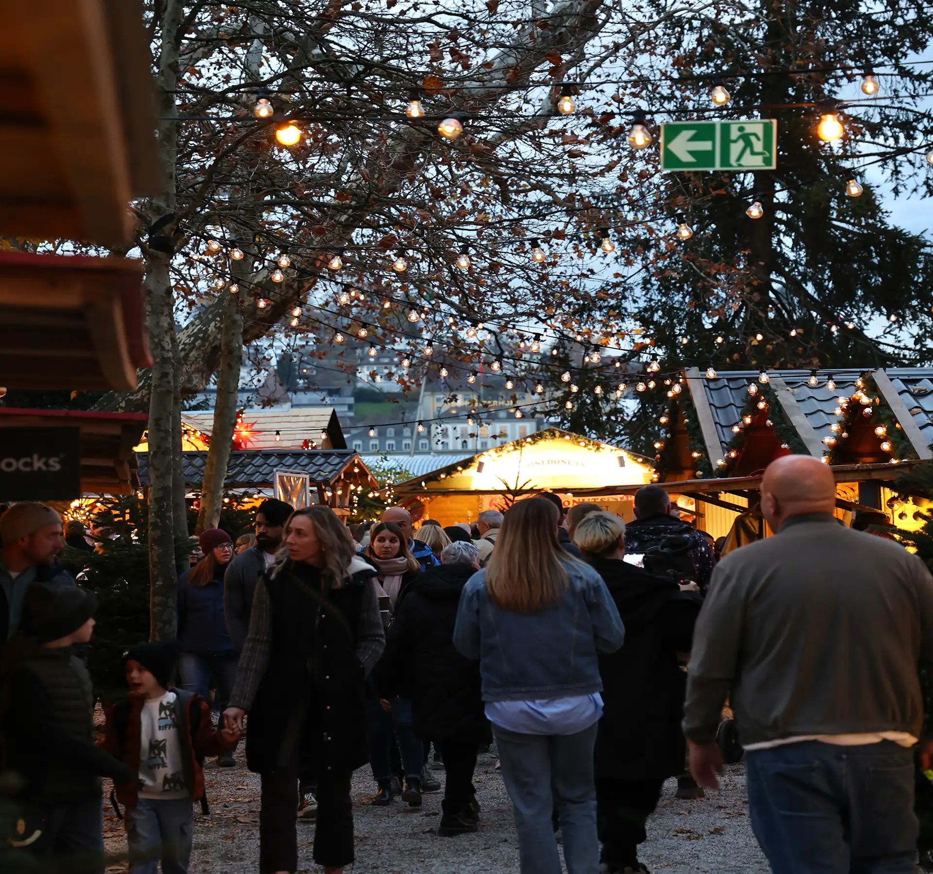 Des gens se promènent entre les stands en bois illuminés d'un marché de Noël, à la lueur du soir.