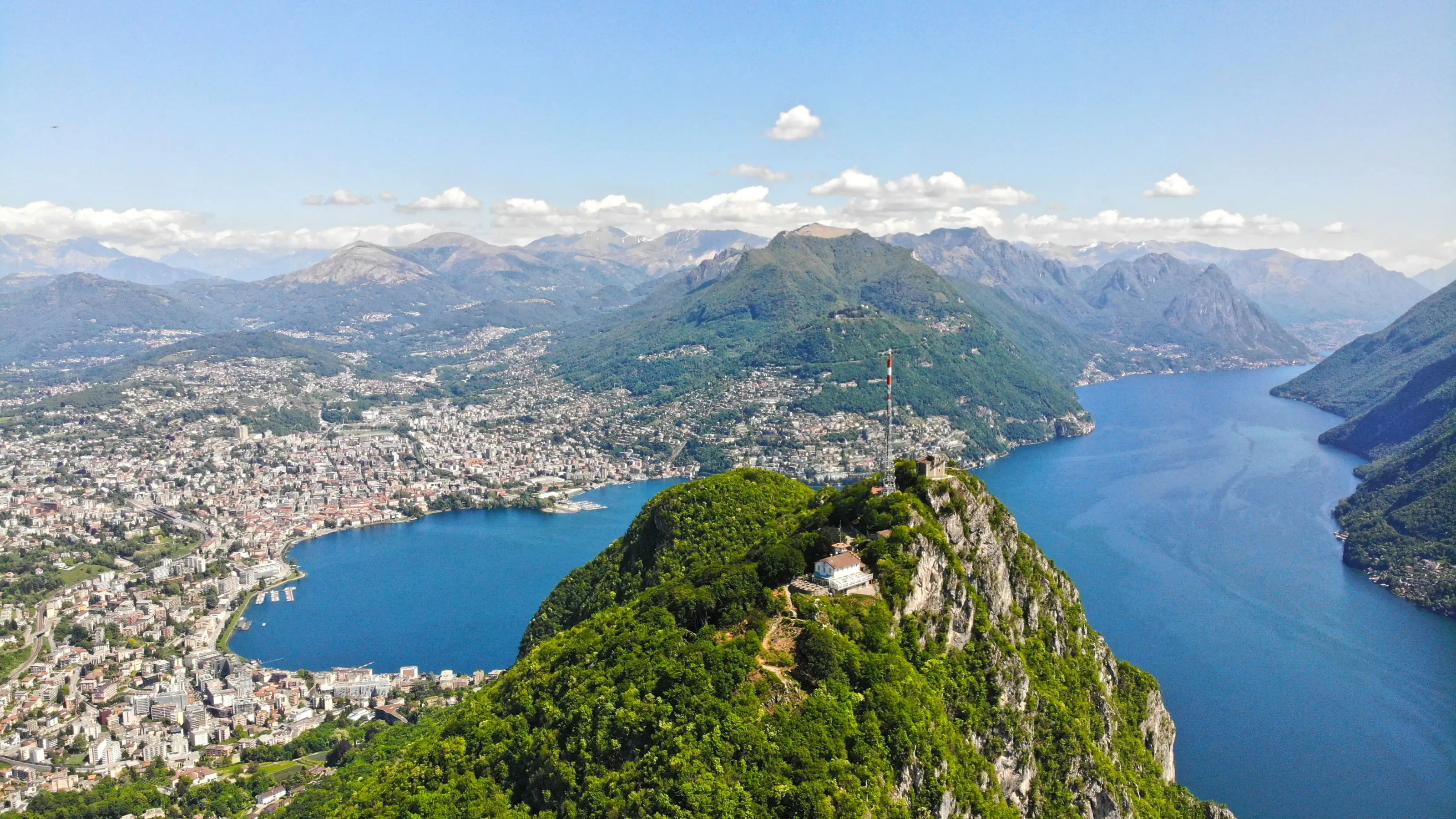 Panoramic view of Lake Lugano surrounded by mountains.