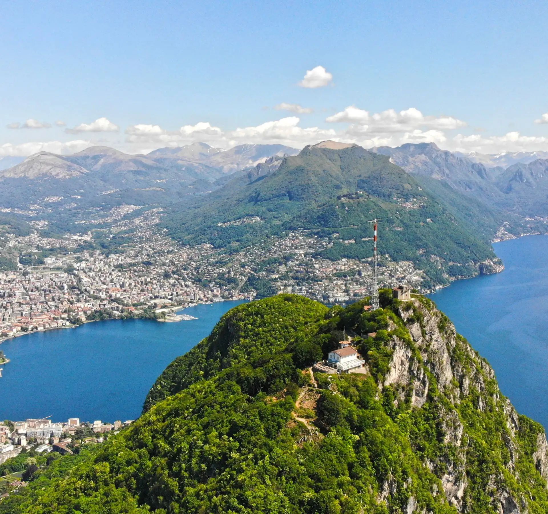Panoramic view of Lake Lugano surrounded by mountains.
