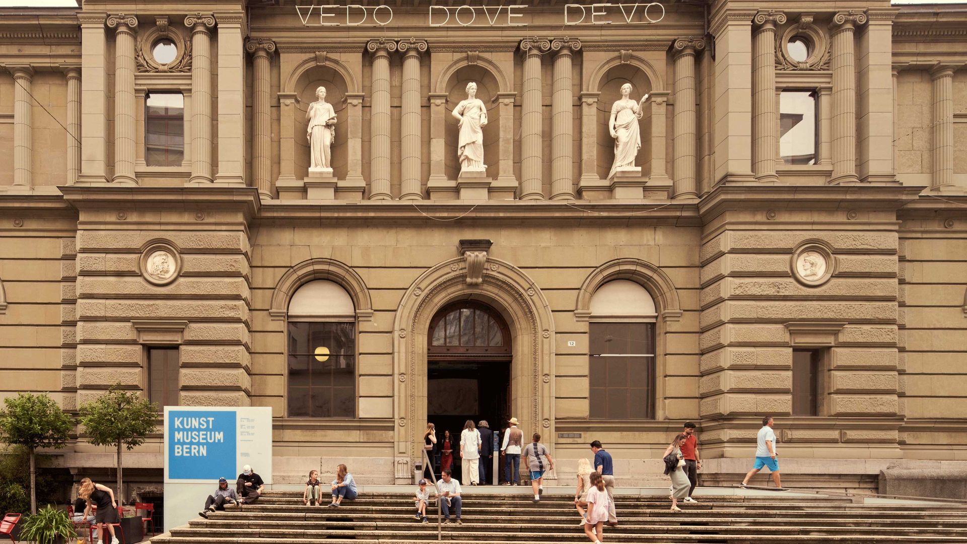 Die Vorderseite eines alten Gebäudes mit einer Treppe, auf der sich Menschen befinden.