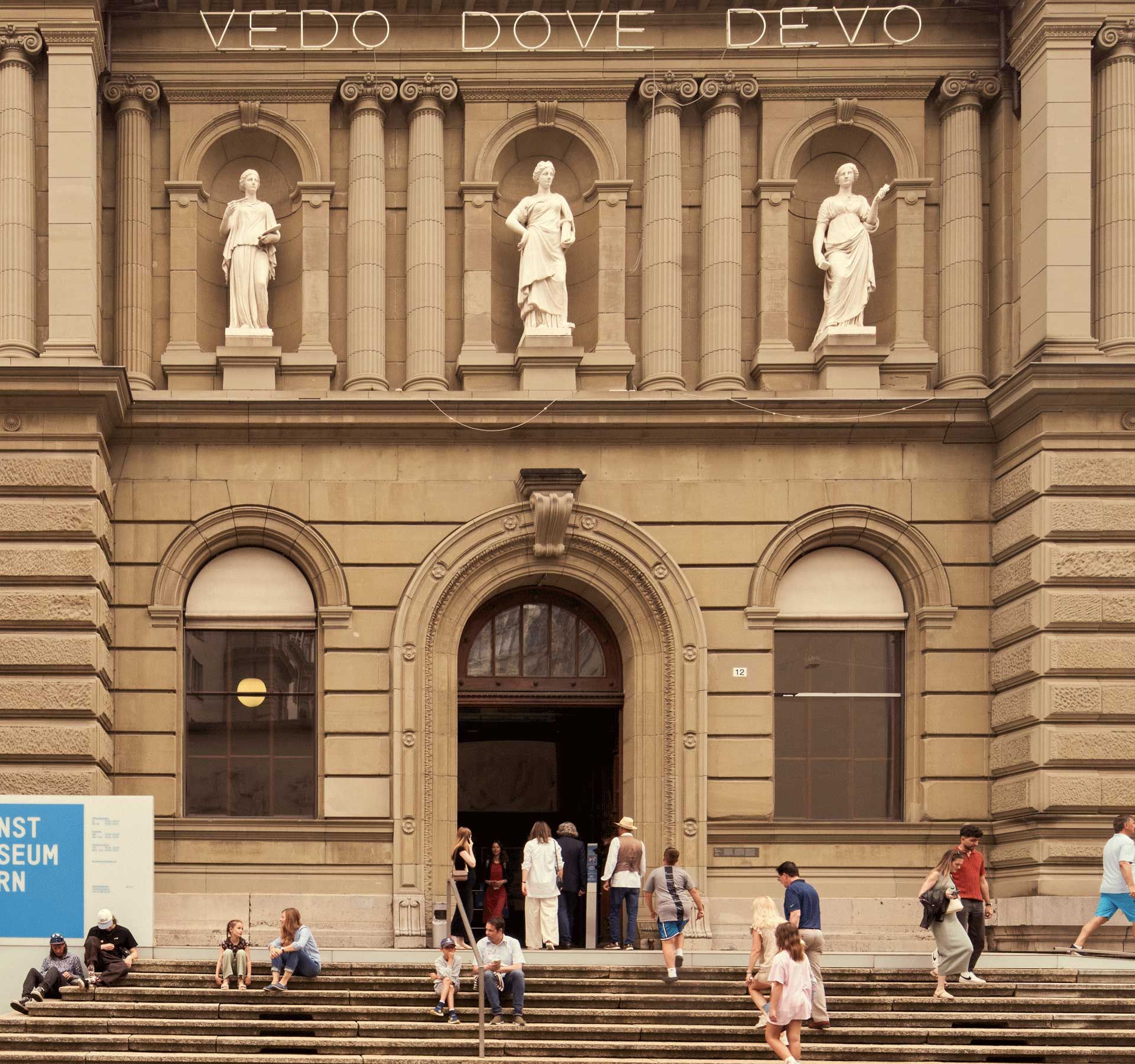 Die Vorderseite eines alten Gebäudes mit einer Treppe, auf der sich Menschen befinden.