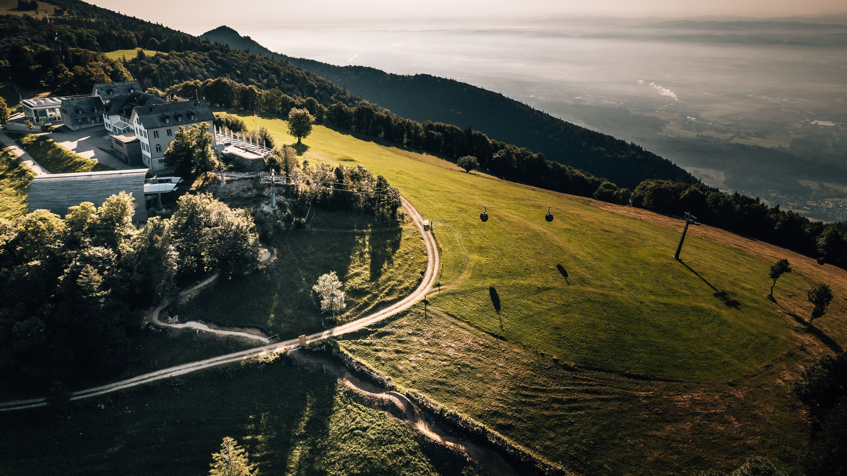 Aerial view of a house on the Weissenstein, surrounded by trees and meadows, with clear skies in the background.